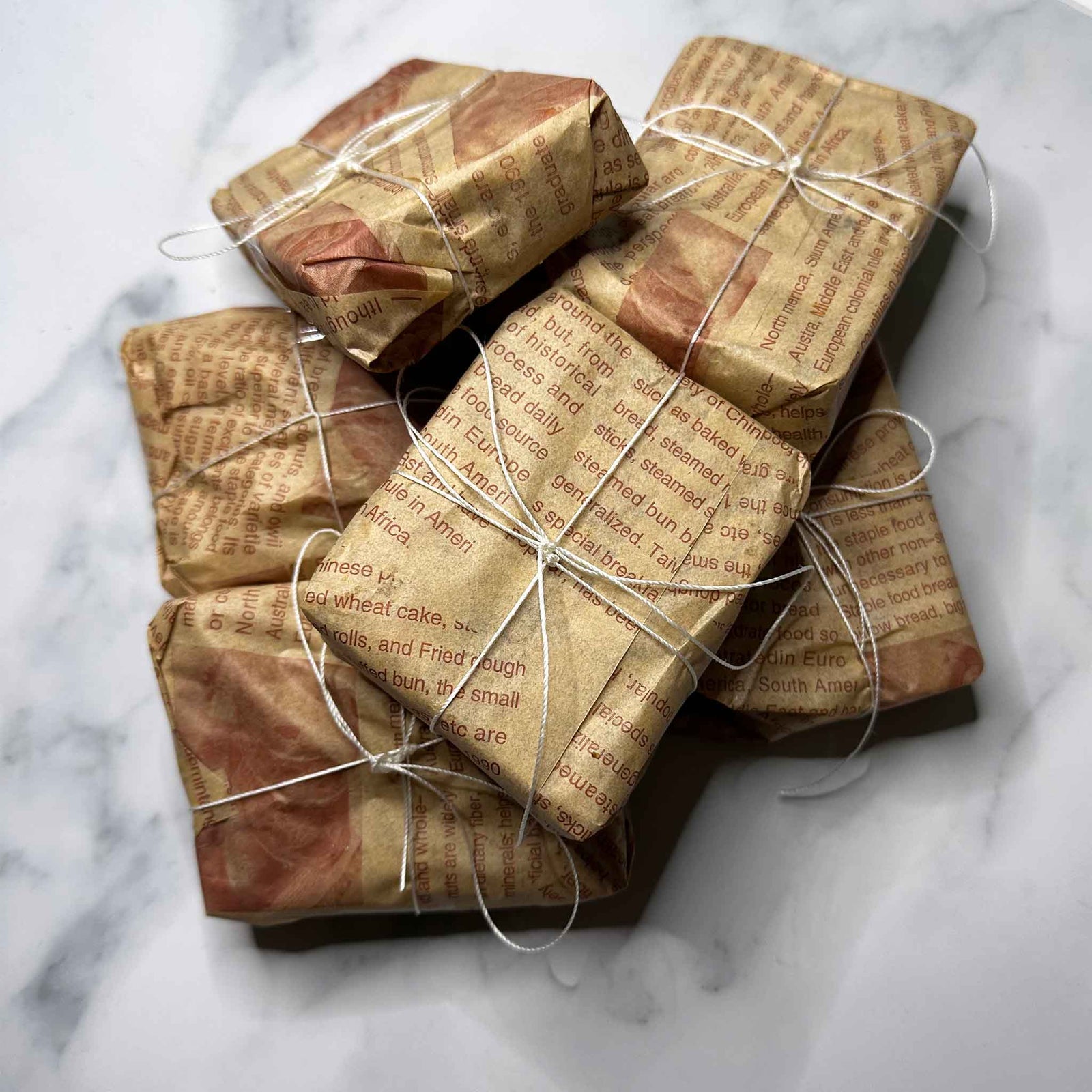 Gifts wrapped black soap in brown paper with string on a marble surface