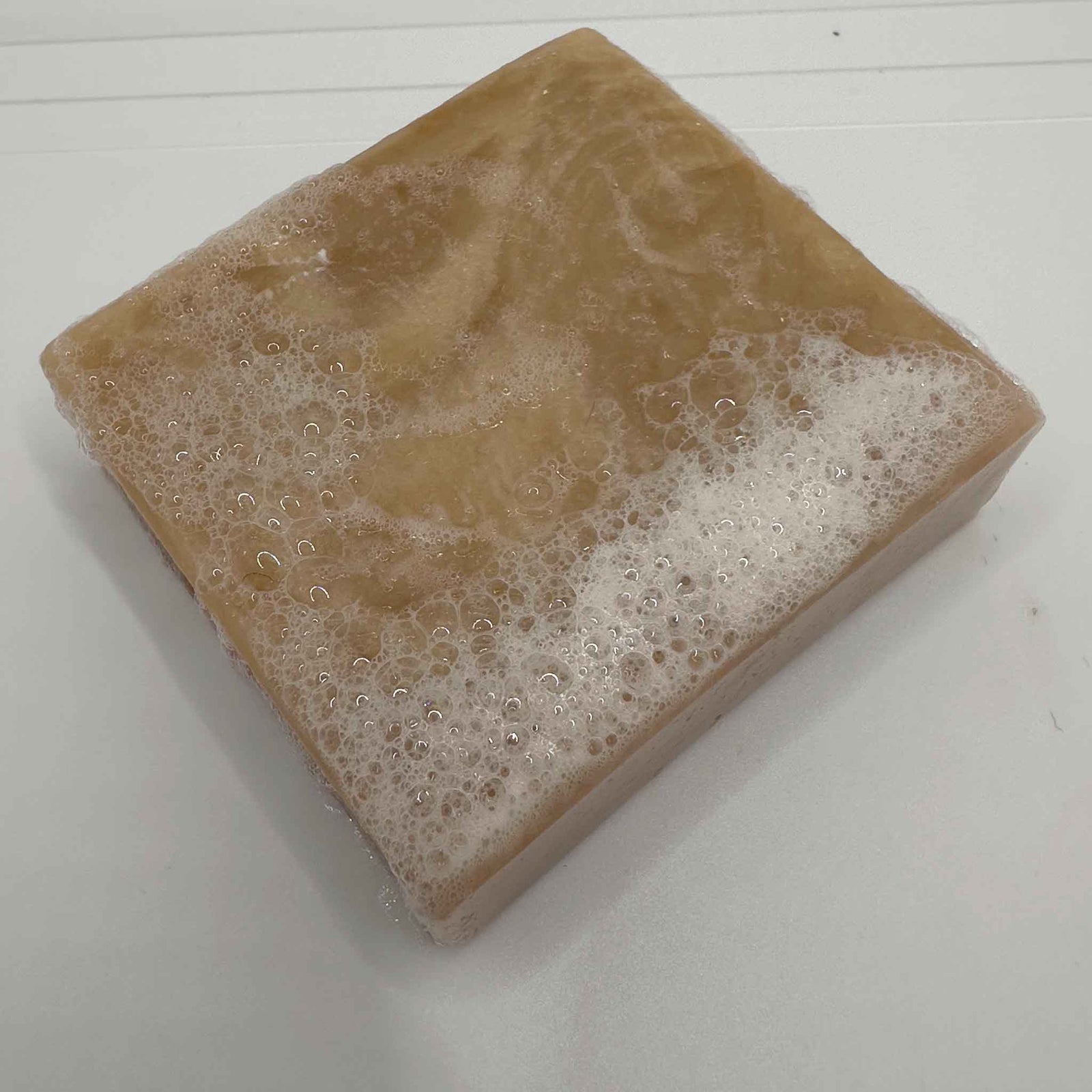 A beige and white soap bar with lather on a white background