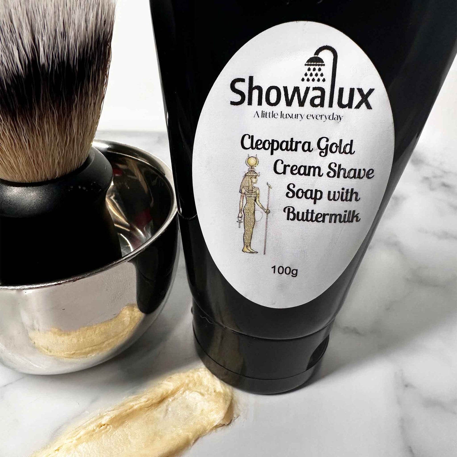 Showalux Cleopatra Gold Cream Shave Soap with Buttermilk on a marble surface with a shaving brush.
