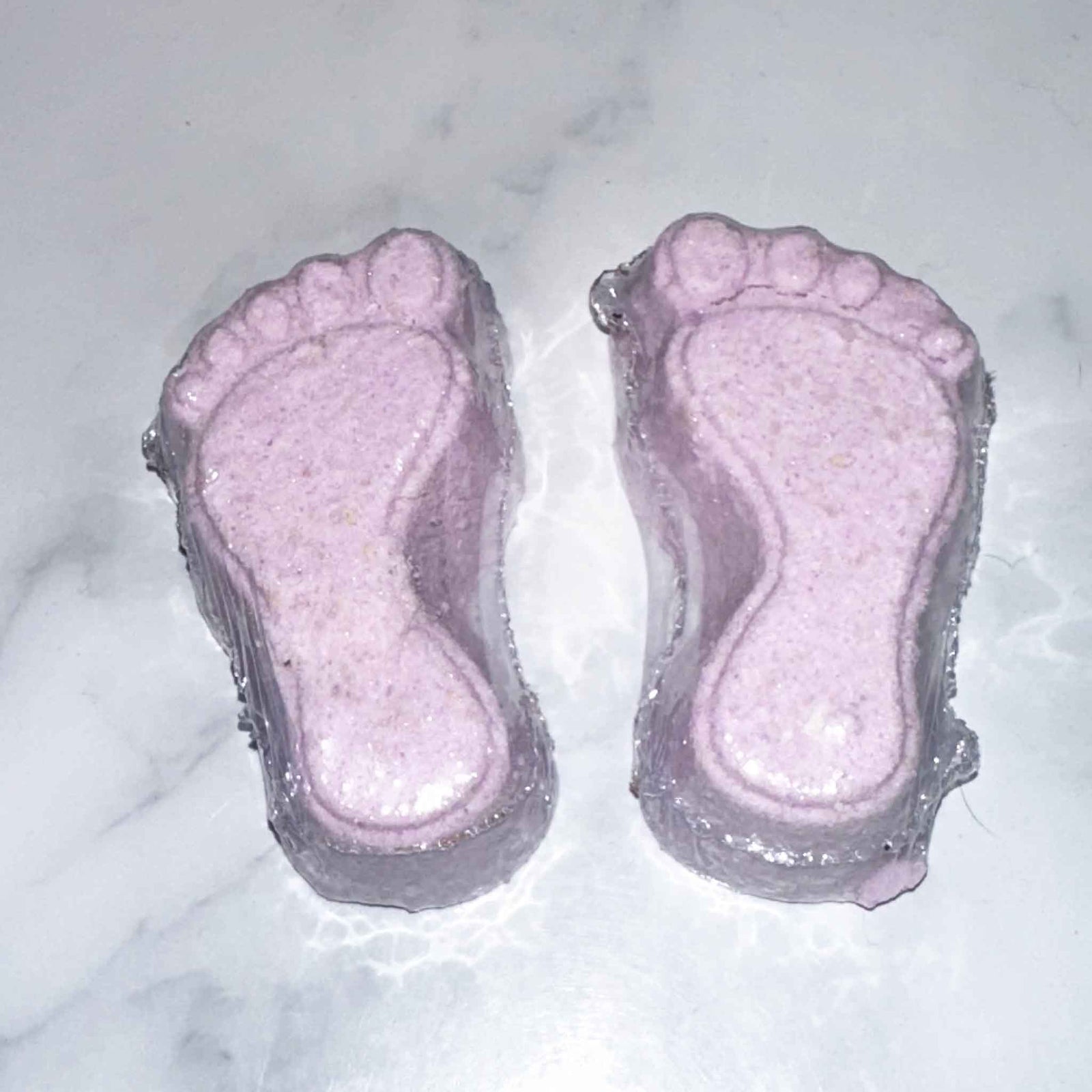 Two pink foot-shaped foot fizzies on a marble surface