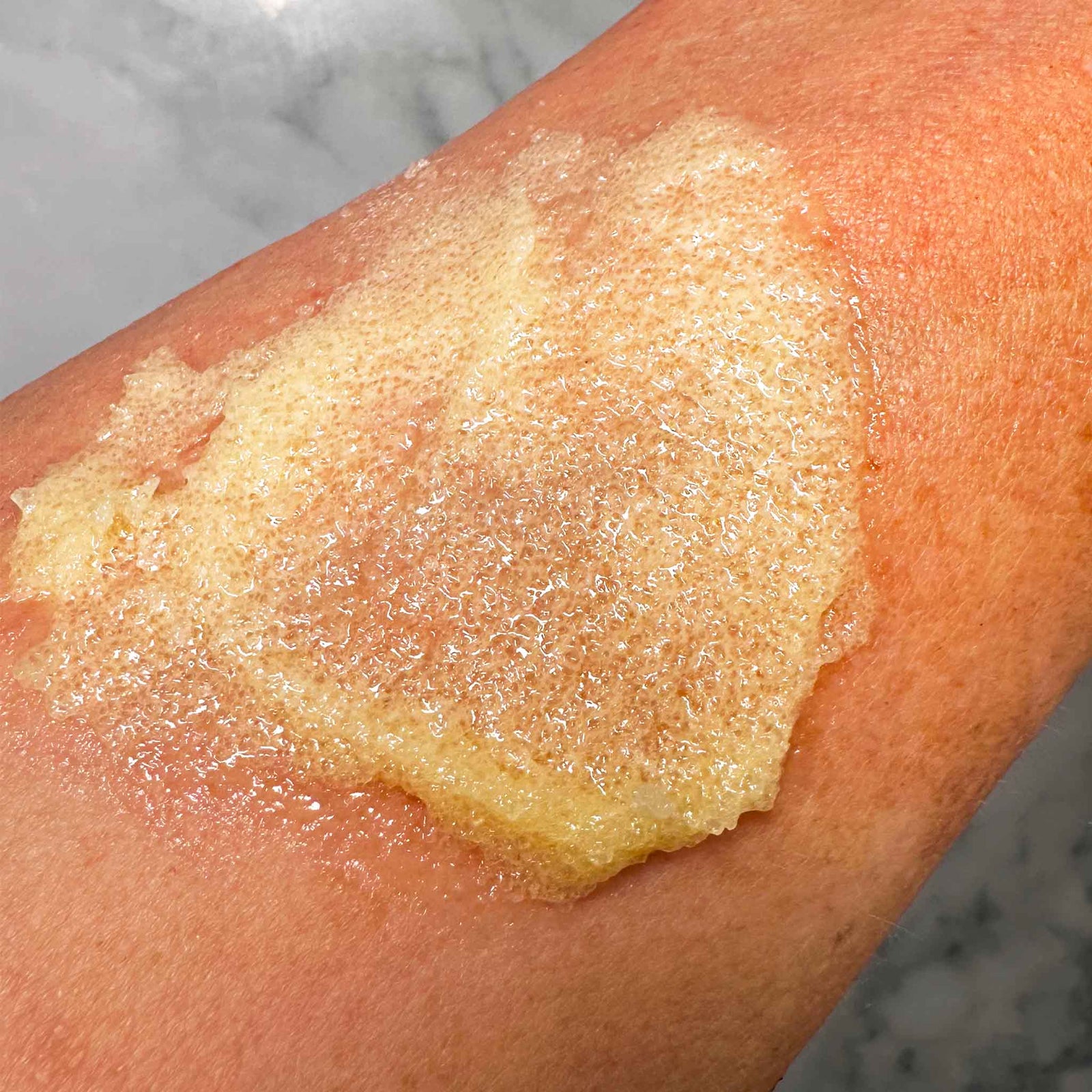 Close-up of a person's arm with a Showalux sugar scrub application on a marble surface.