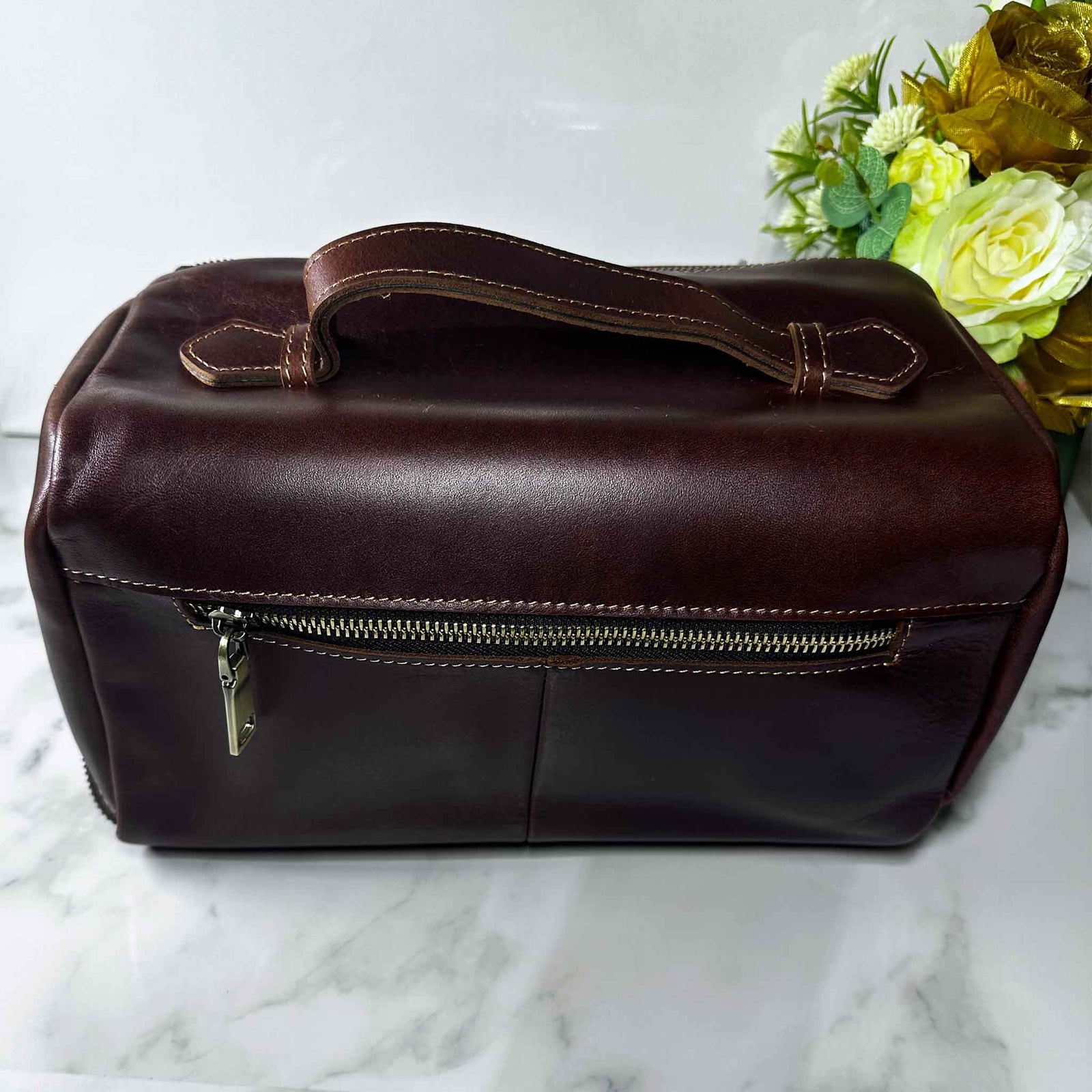 Brown leather bag on a marble surface with flowers in the background