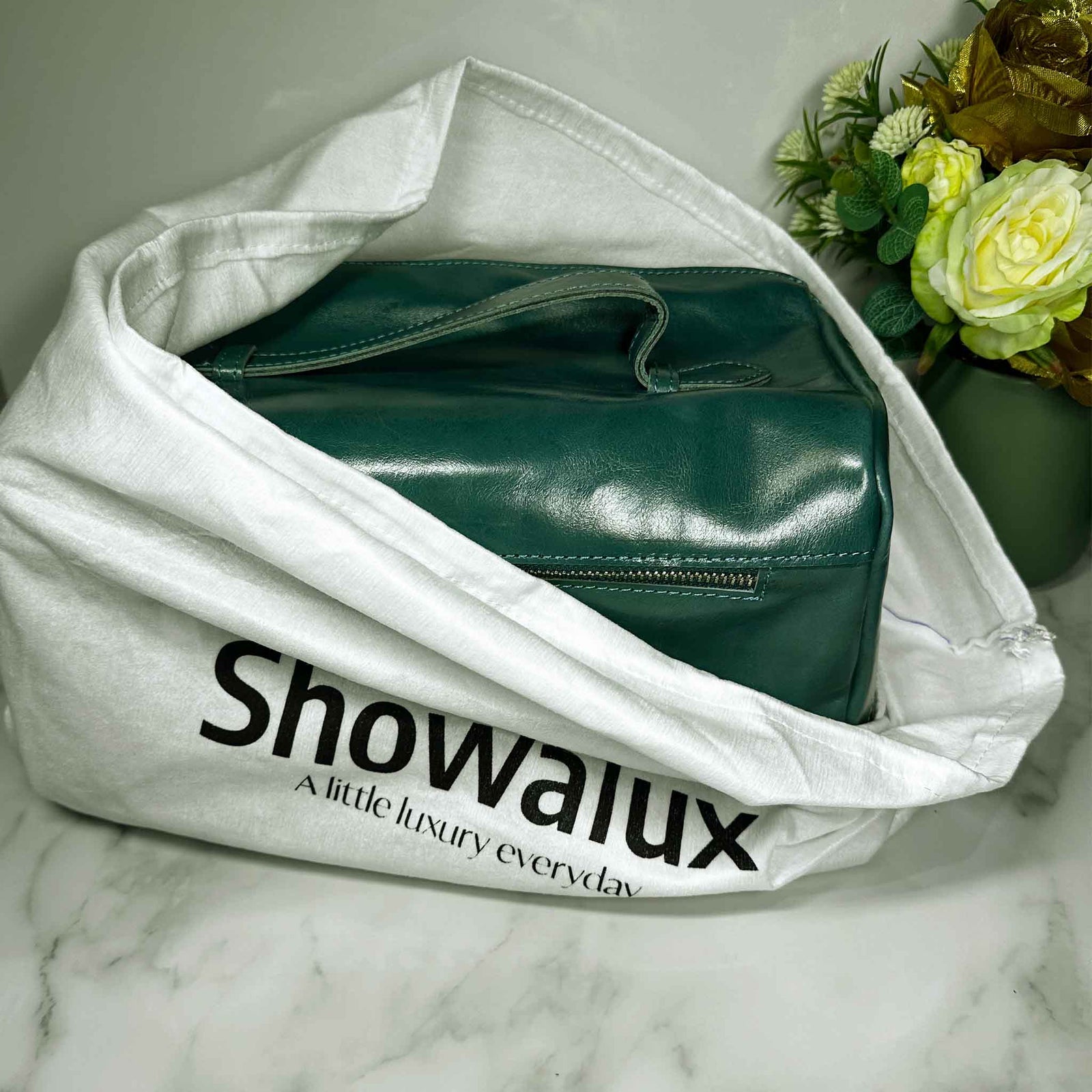 Green handbag inside a white Showalux bag on a marble surface with flowers in the background.