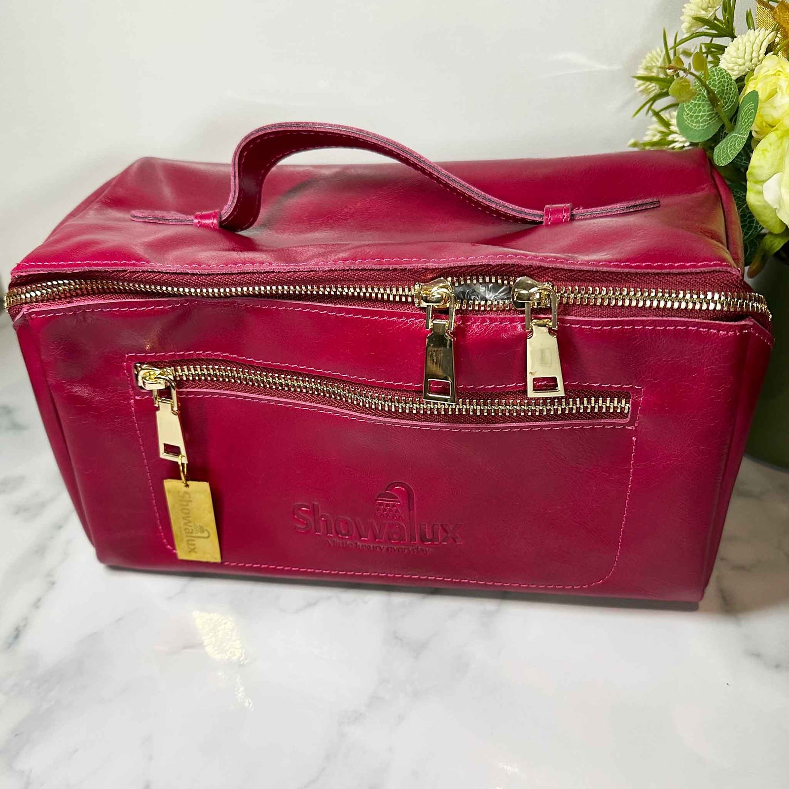 Pink travel bag with gold zippers on a marble surface with flowers in the background