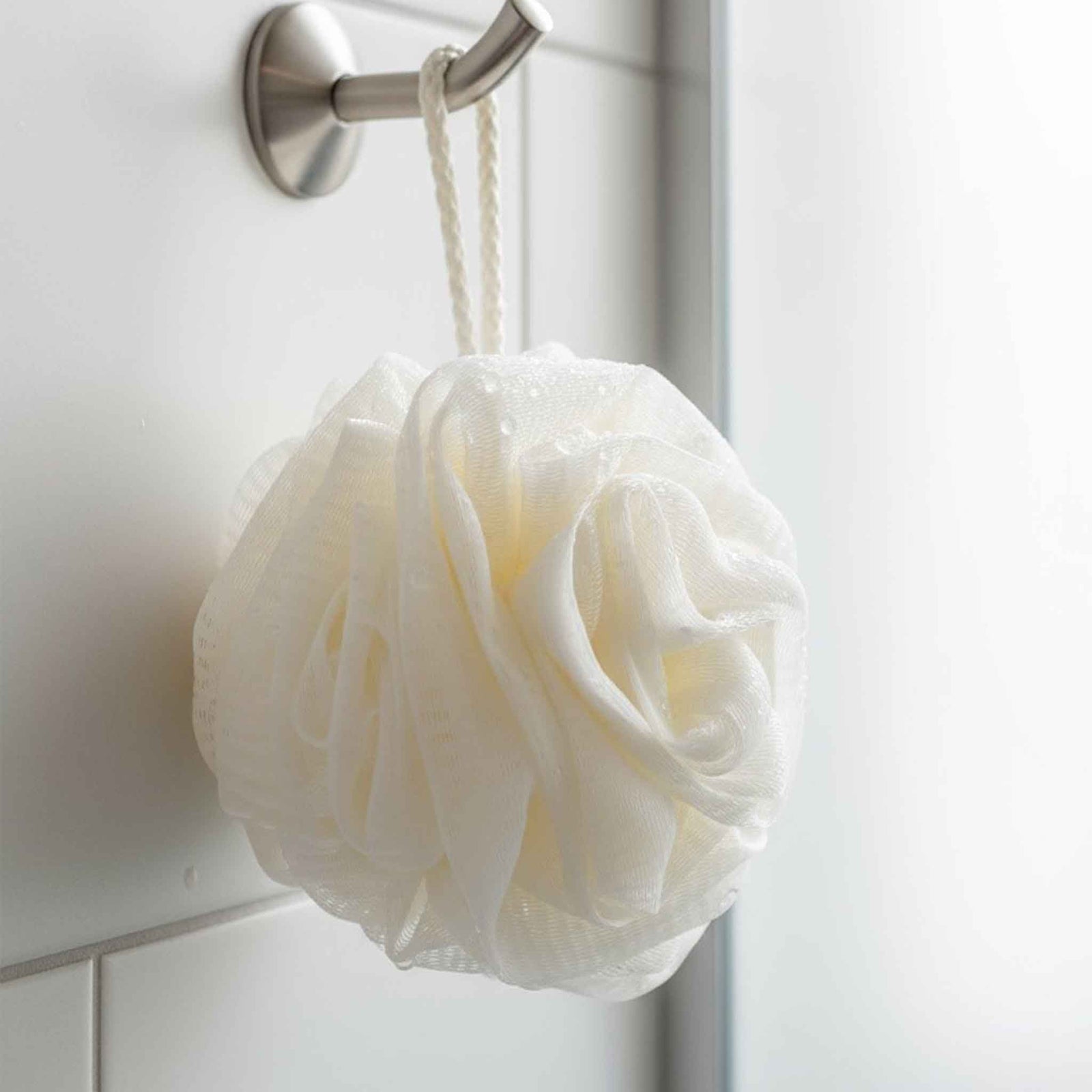 White bath pouf hanging on a hook against a bathroom wall.