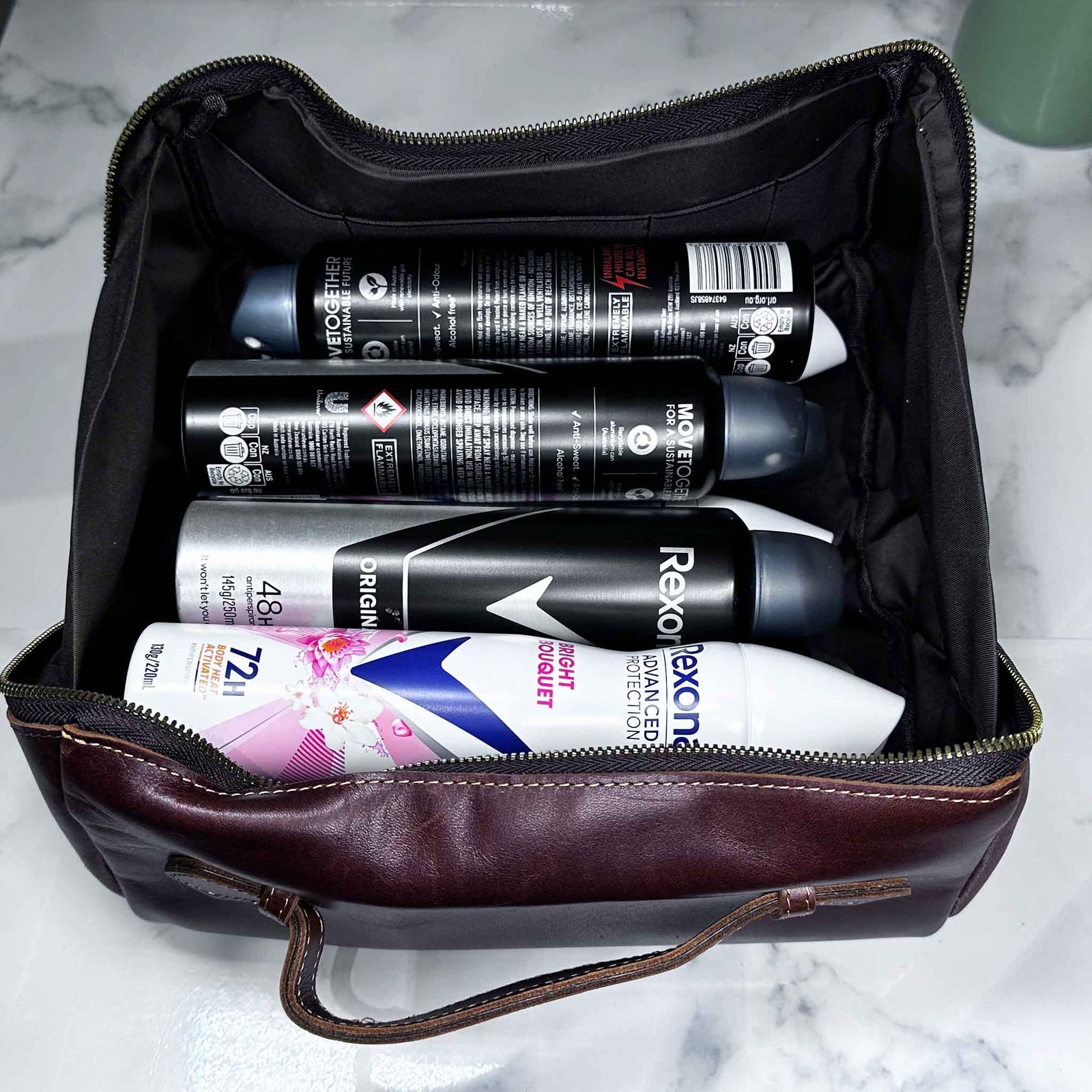 Cosmetic bag filled with deodorant cans on a marble surface
