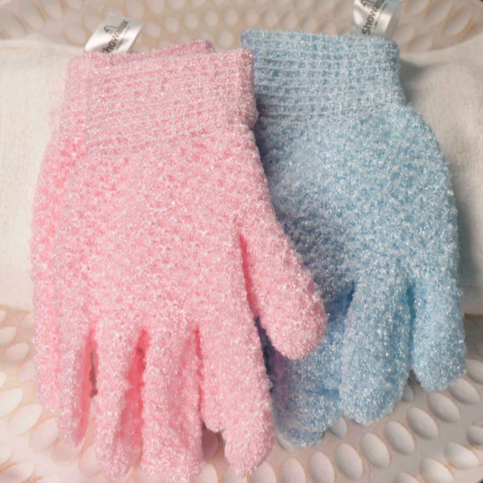 A pair of baby blue exfoliating gloves, with a pair of baby pink exfoliating gloves on a white textured background
