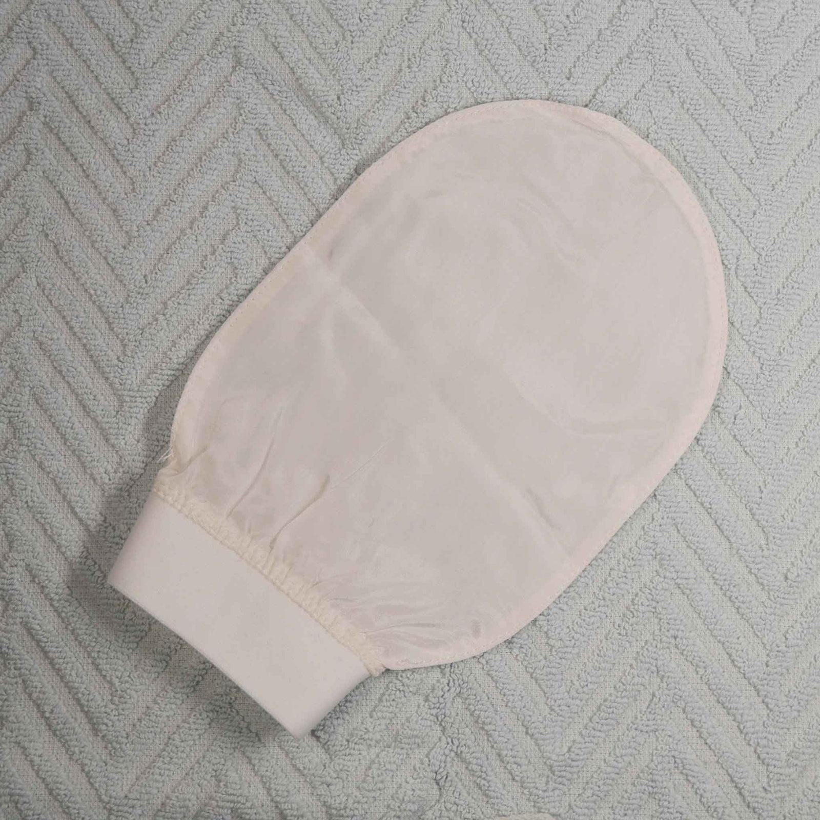 shows a hand mitten type of glove that is made out of off white raw silk with a cotton band on a background of a light blue towel