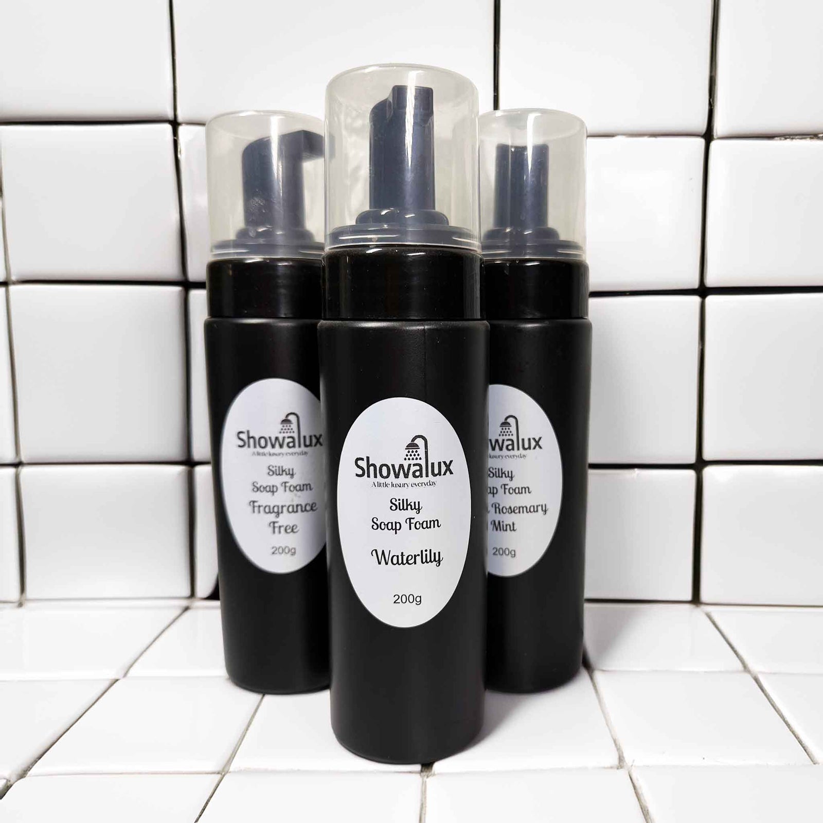 Three Showalux soap foam bottles on a tiled bathroom floor.