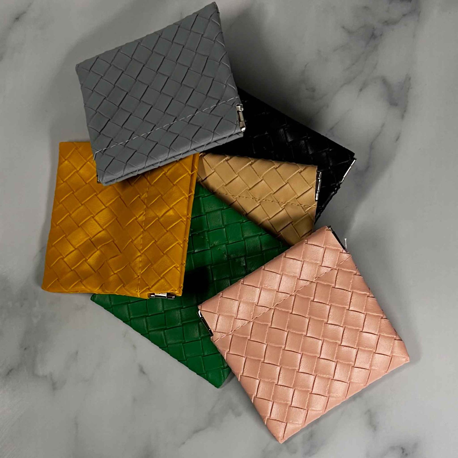 Collection of woven PU leather Showalux personal bags in various colors on a marble surface