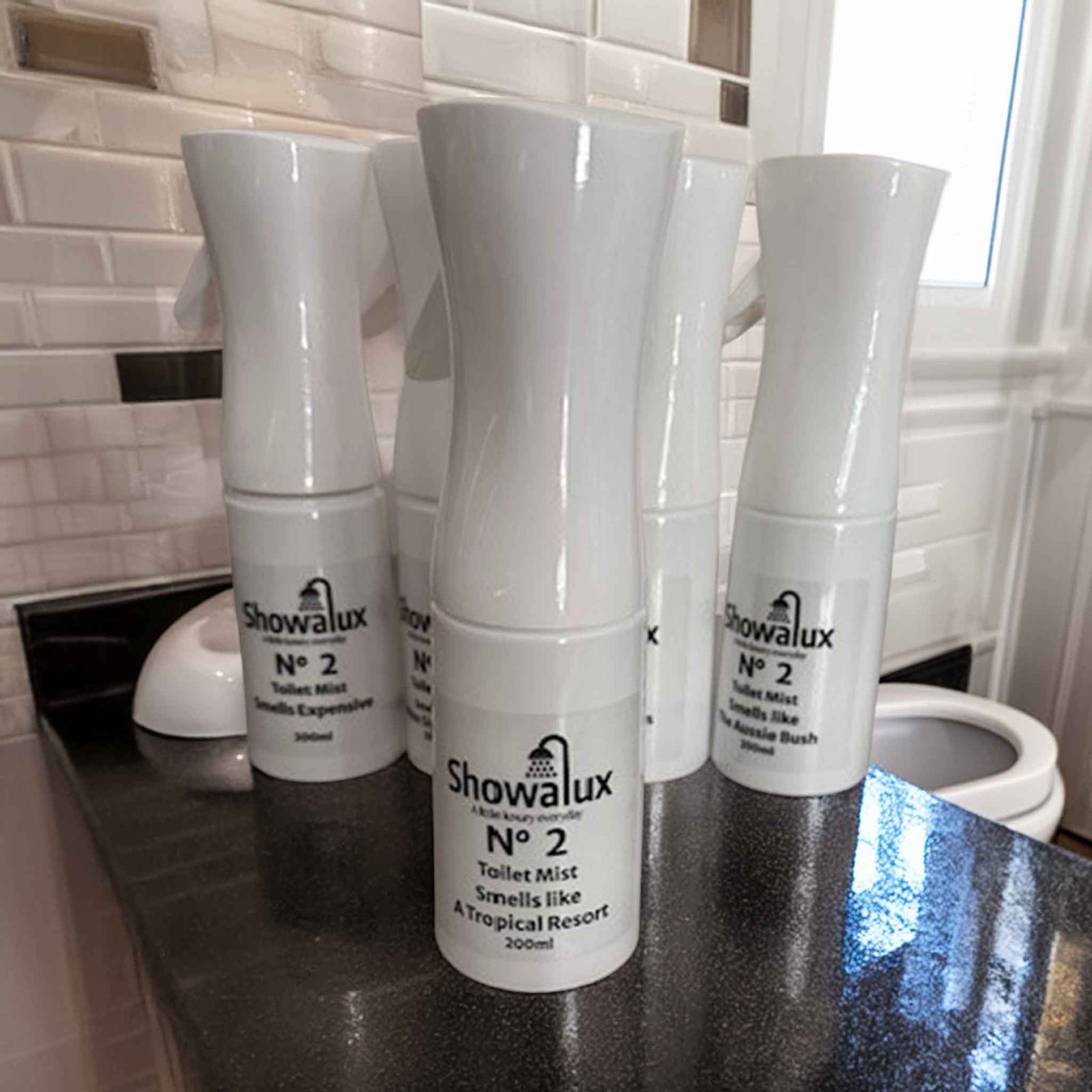 Showalux toilet mist in "Smells like A Tropical Resort" on a bathroom counter with tiled wall in the background