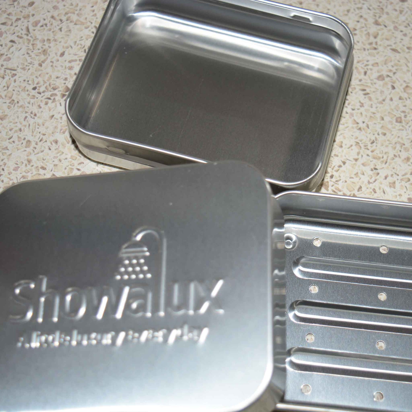 Aluminium soap container with lid half off, showing a soap inside, with 3 soap containers in the background