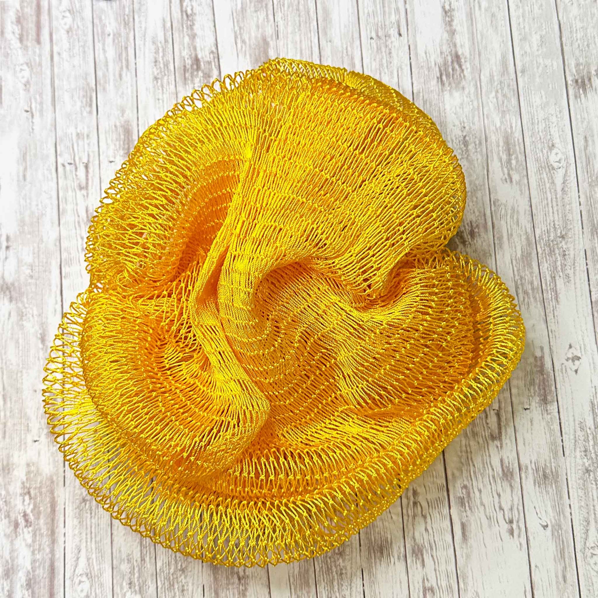 A coil of African Net Sponge coloured yellow on a white background