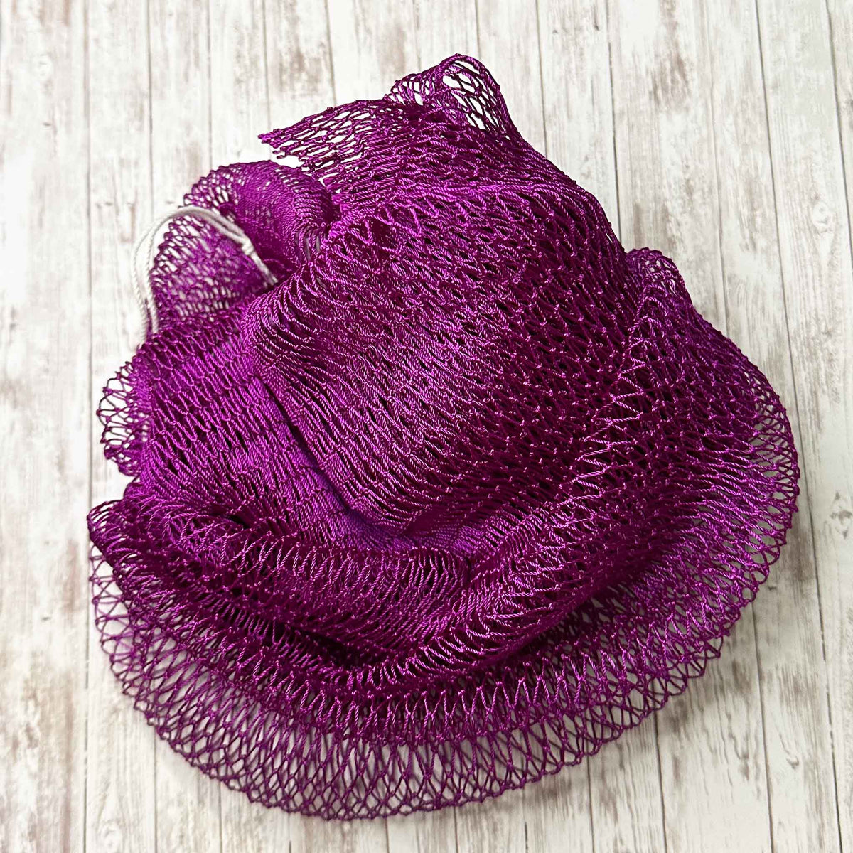 A coil of African Net Sponge coloured Maroon on a white background