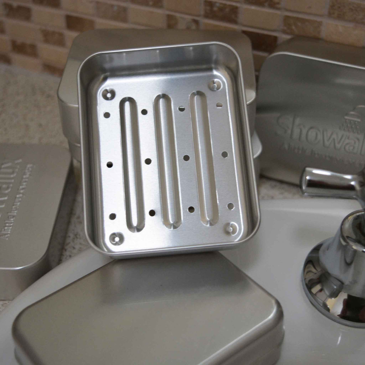 Aluminium soap container base showing drainage holes. Propped up on the lids of 3 other tins
