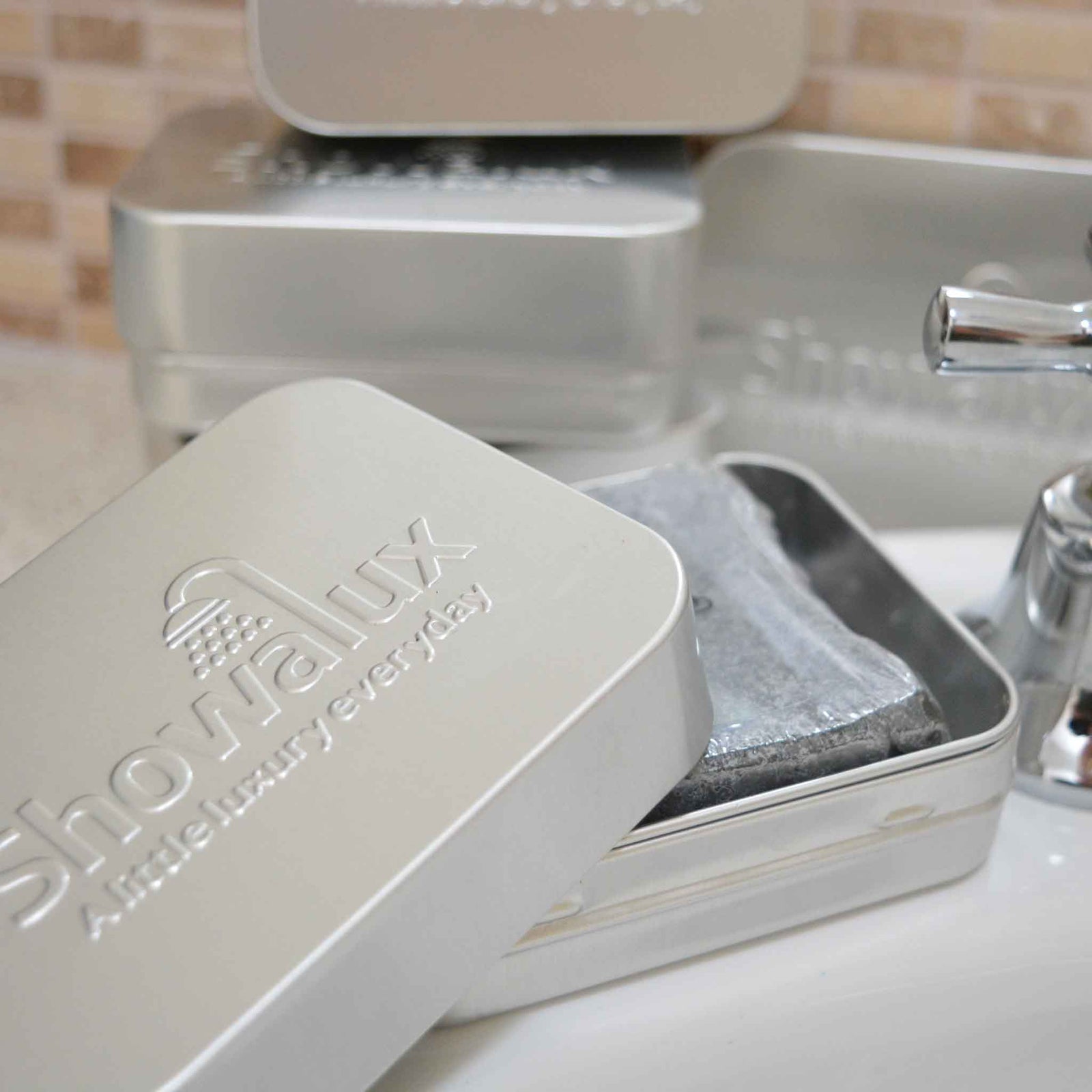 Aluminium soap container with lid half off, showing a soap inside, with 3 soap containers in the background