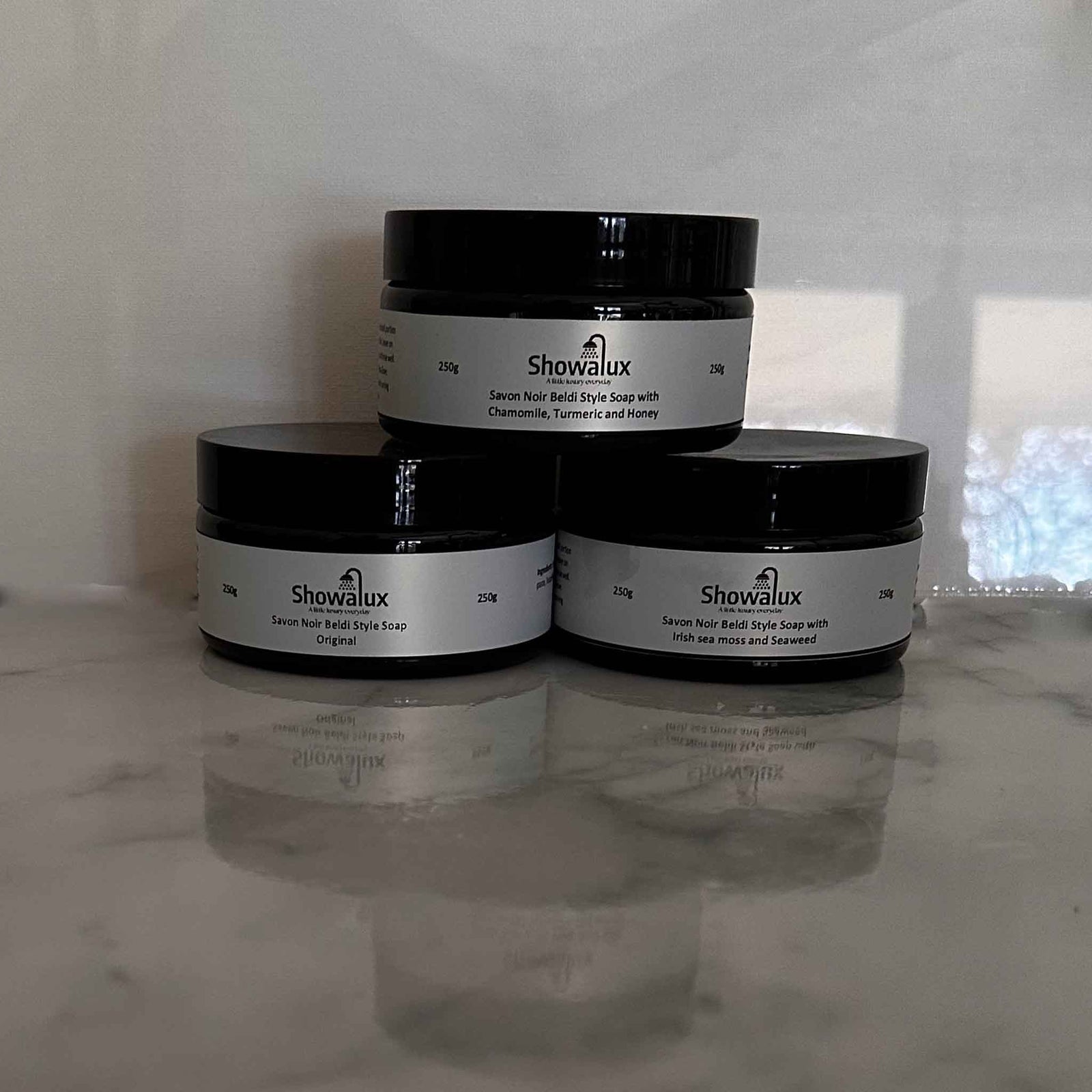 Three stacked jars of Beldi soap with silver labels on a marble top