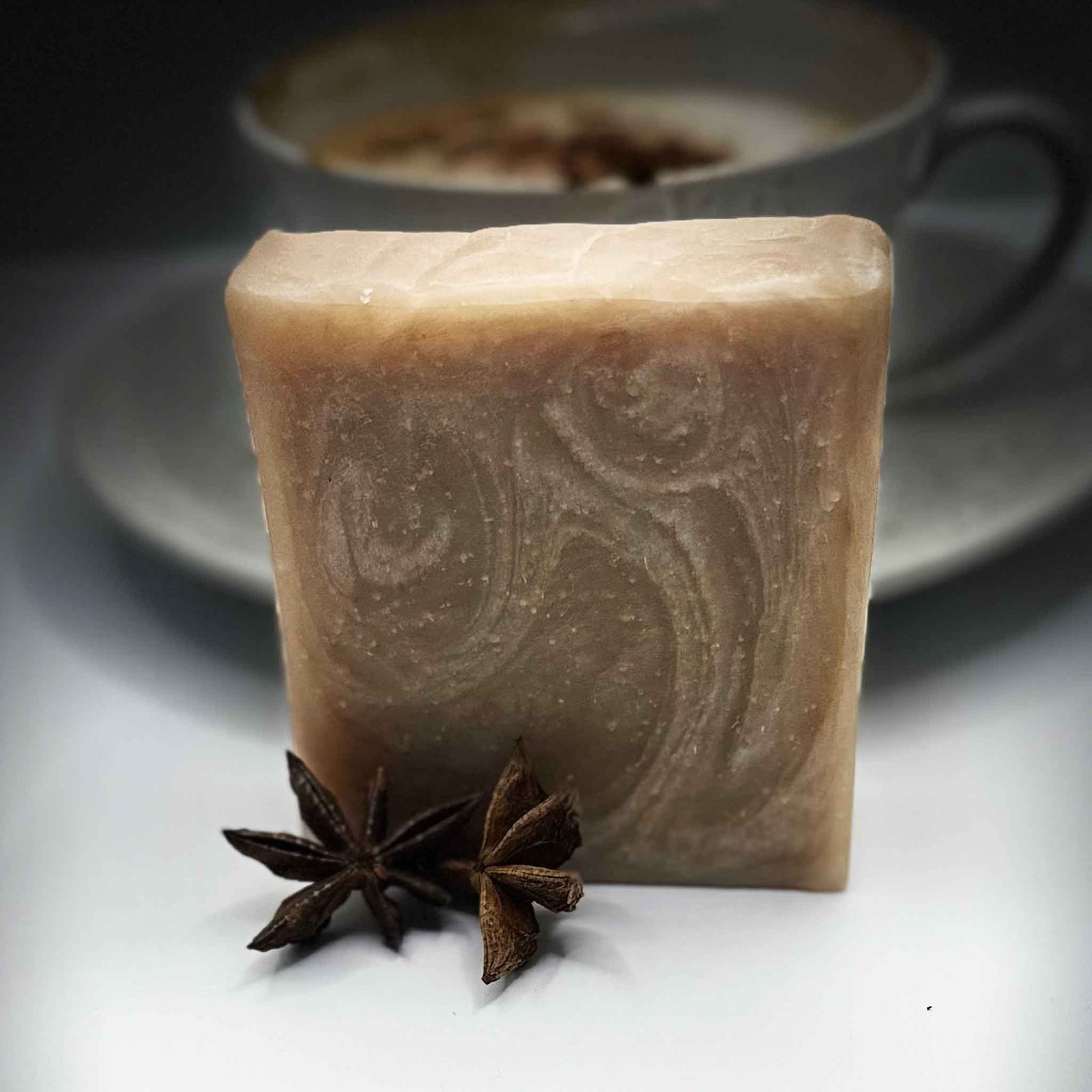 A beige and white soap with 2 star anise in front and a tea up in the background