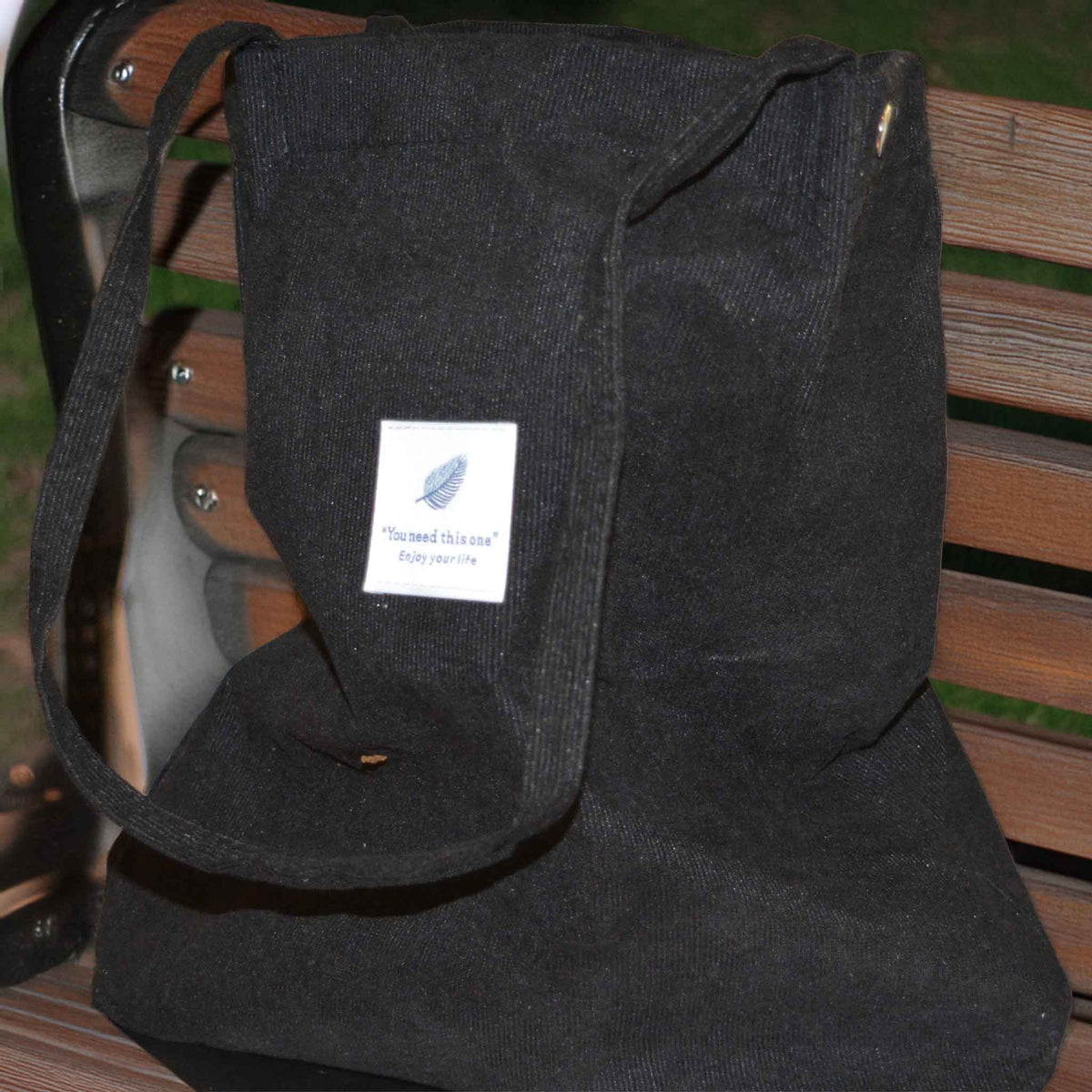 A black corduroy tote bag with long handles on a background of a park bench