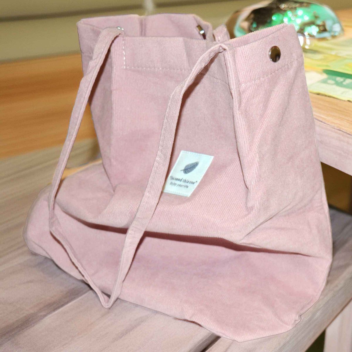 A pink corduroy tote bag with long handles on a background of a table 