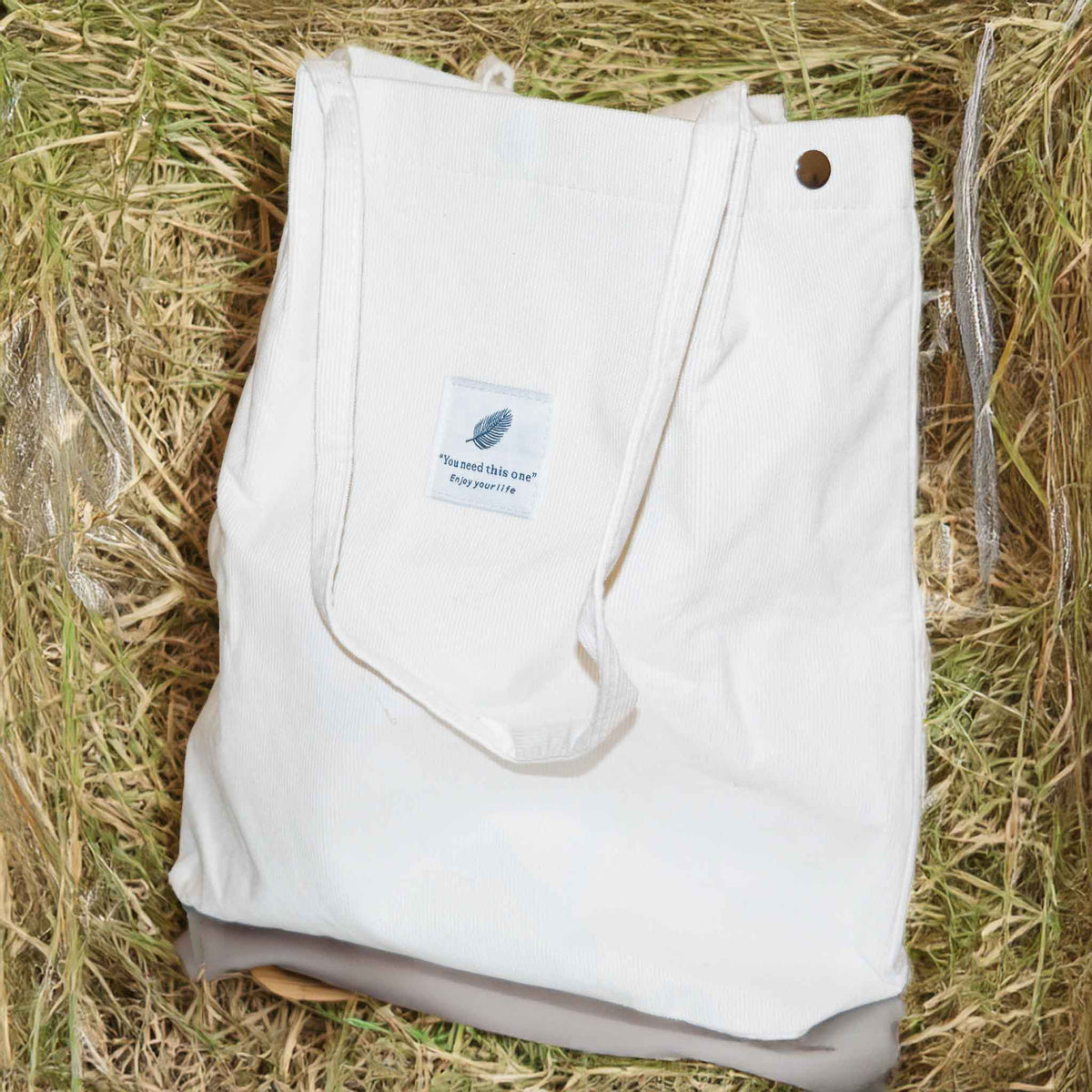 A white tote bag with long handles, on a background of hay.