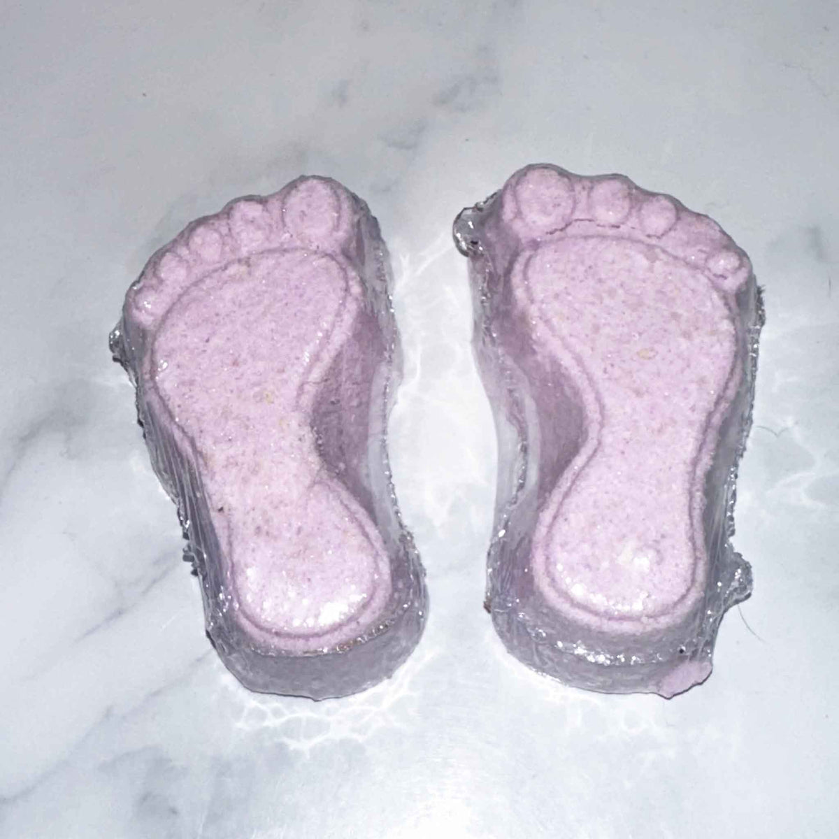 Two pink foot-shaped foot fizzies on a marble surface