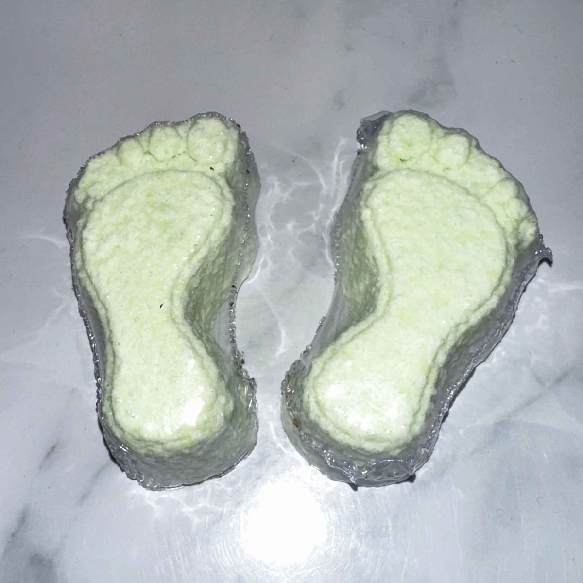Two green footprints that are foot fizzies on a white marble surface