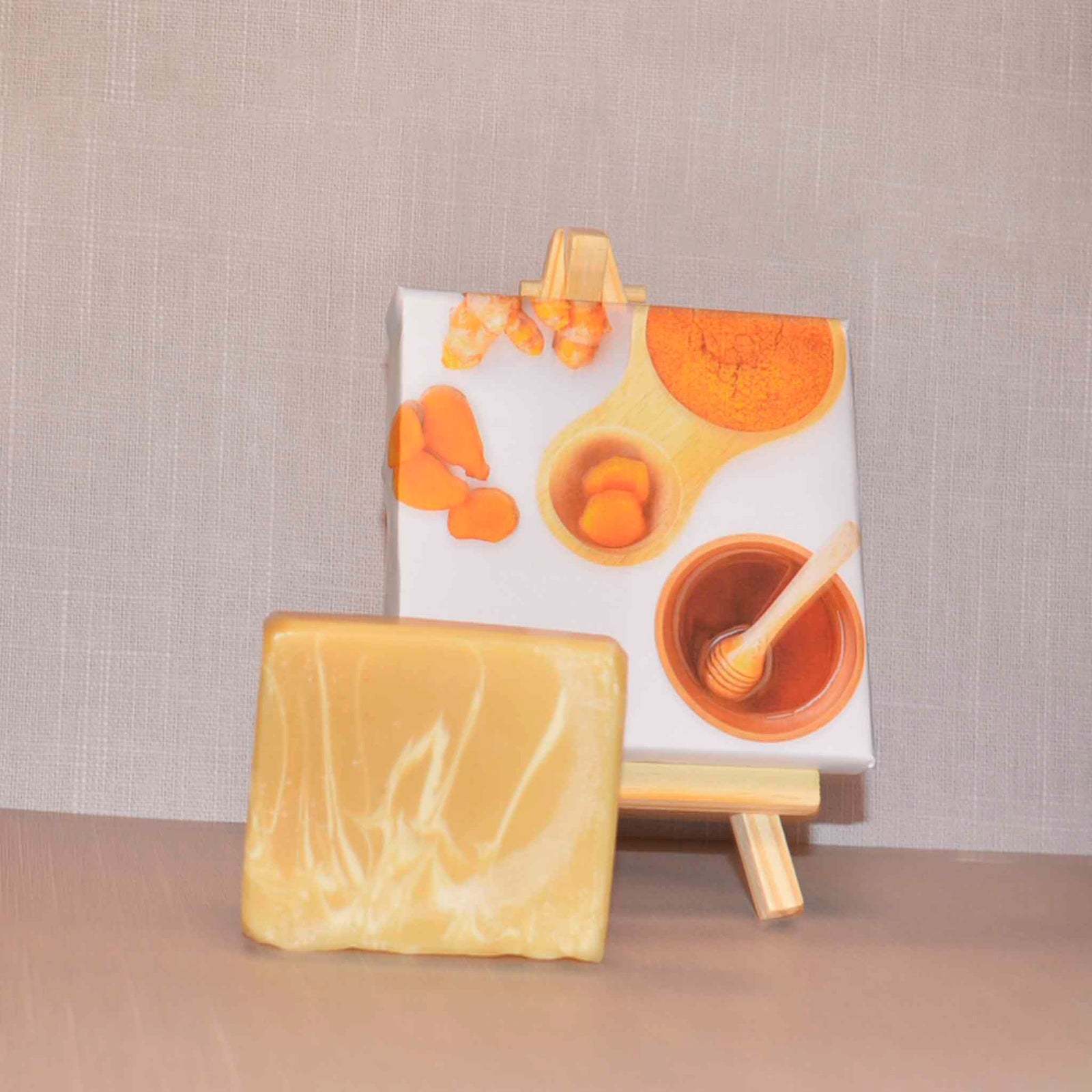 Beige and white bar soap with a picture of honey and turmeric in the background on an easel 
