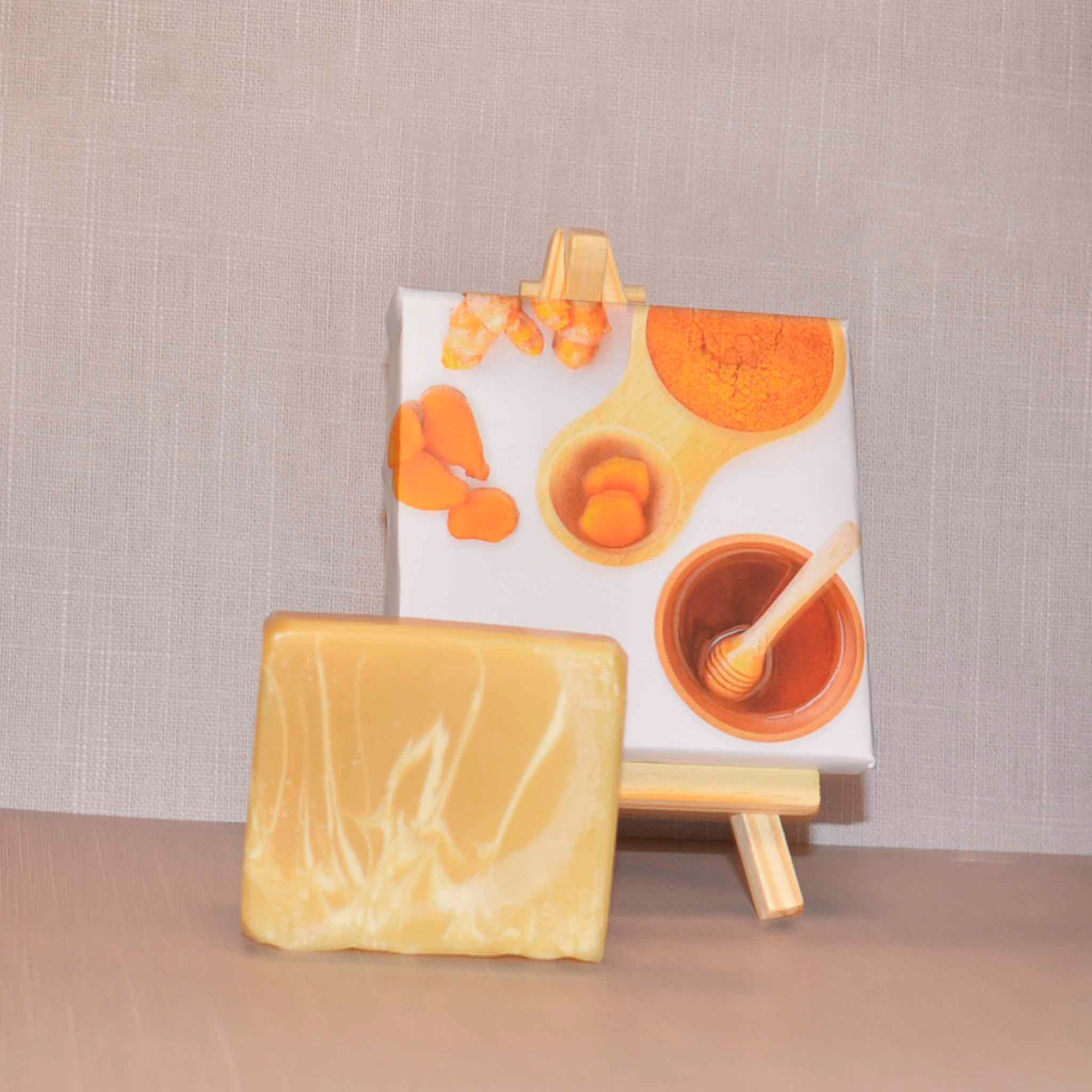 Beige and white bar soap with a picture of honey and turmeric in the background on an easel 