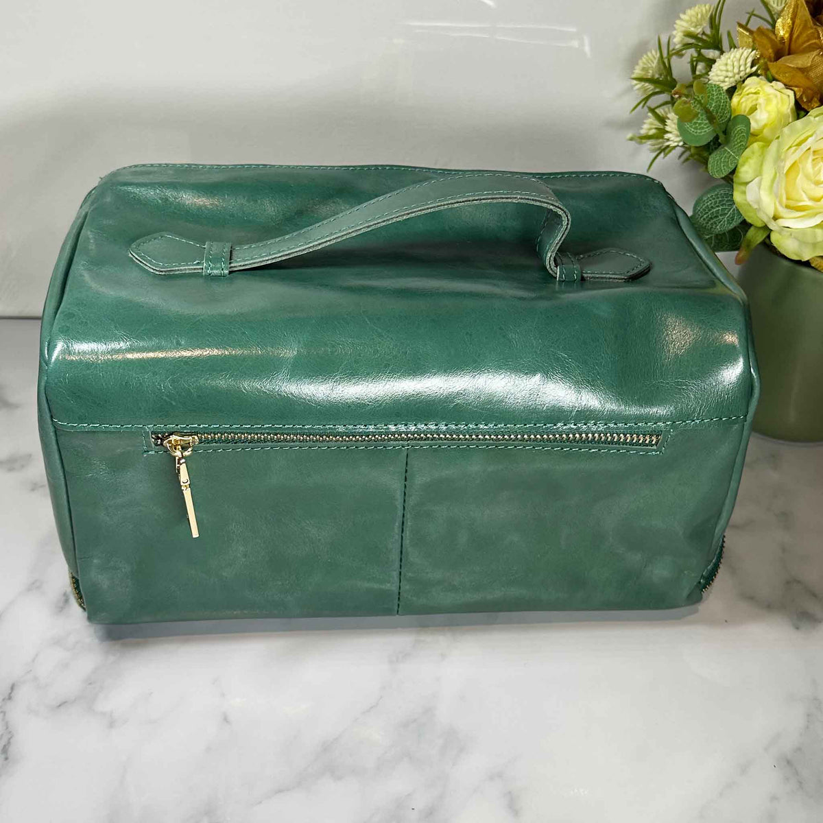 Green leather bag on a marble surface with flowers in the background