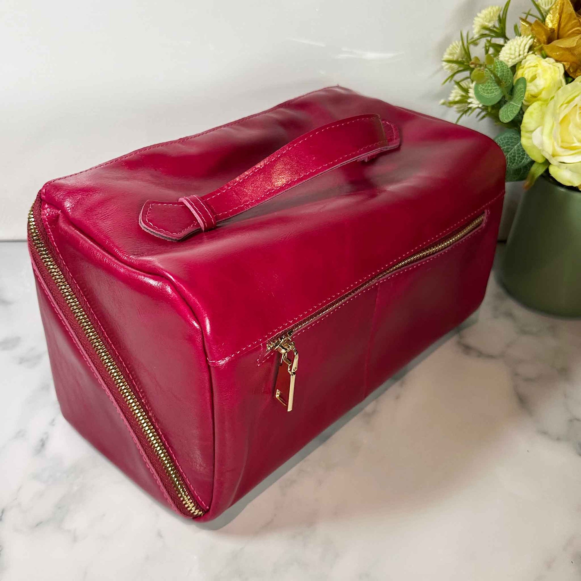 Pink travel bag with gold zippers on a marble surface with flowers in the background