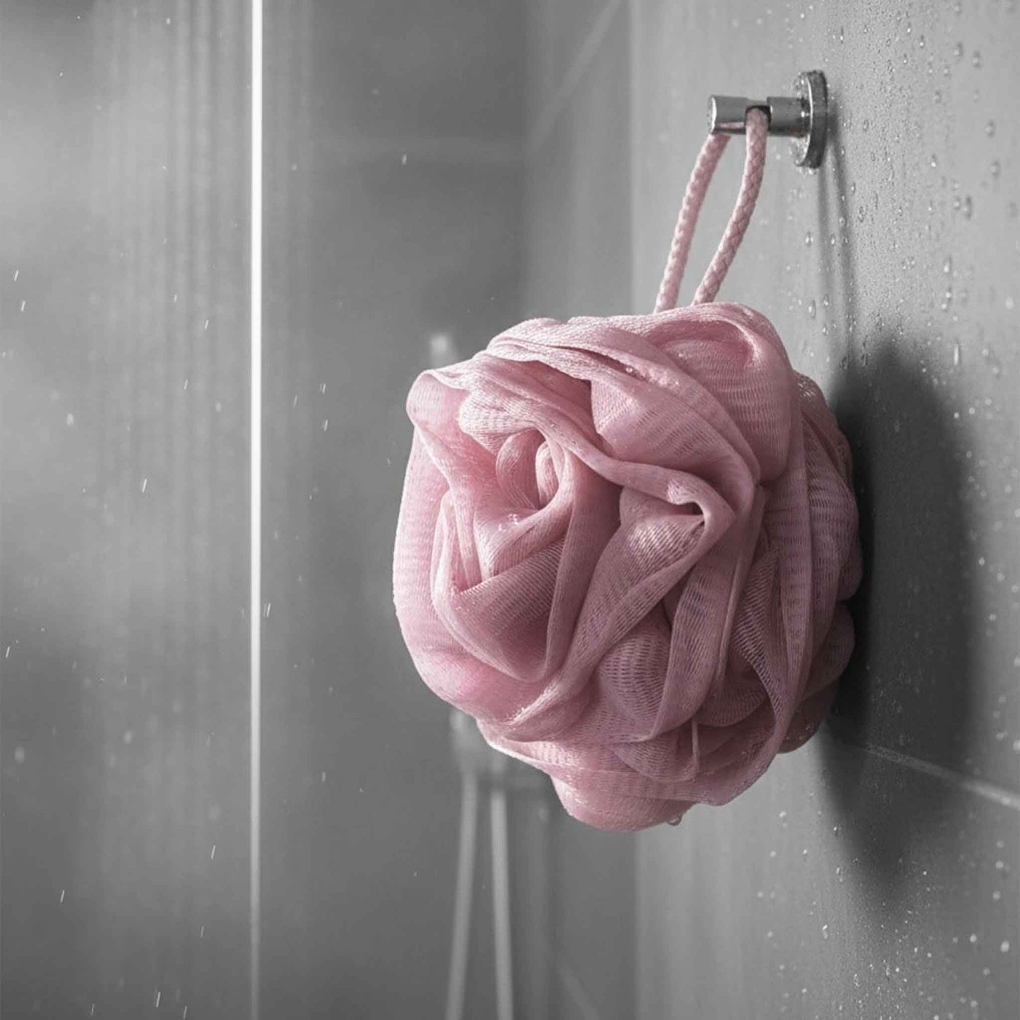 Pink bath pouf hanging on a shower door