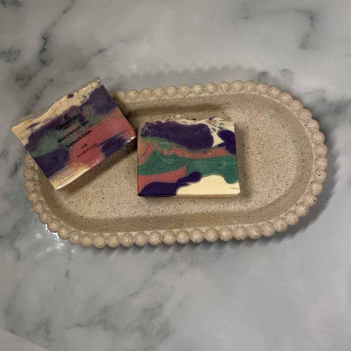Purple, pink, green and white patch coloured soap on a beige background, and a wrapped version