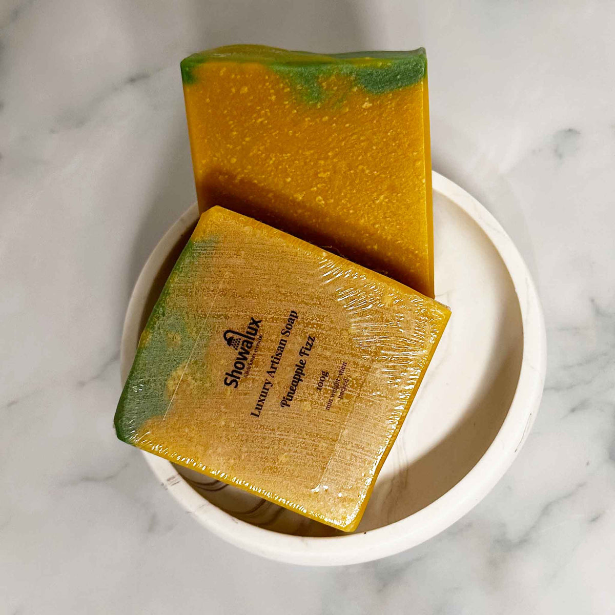 A yellow bar of soap with a green top and a wrapped soap on a white background