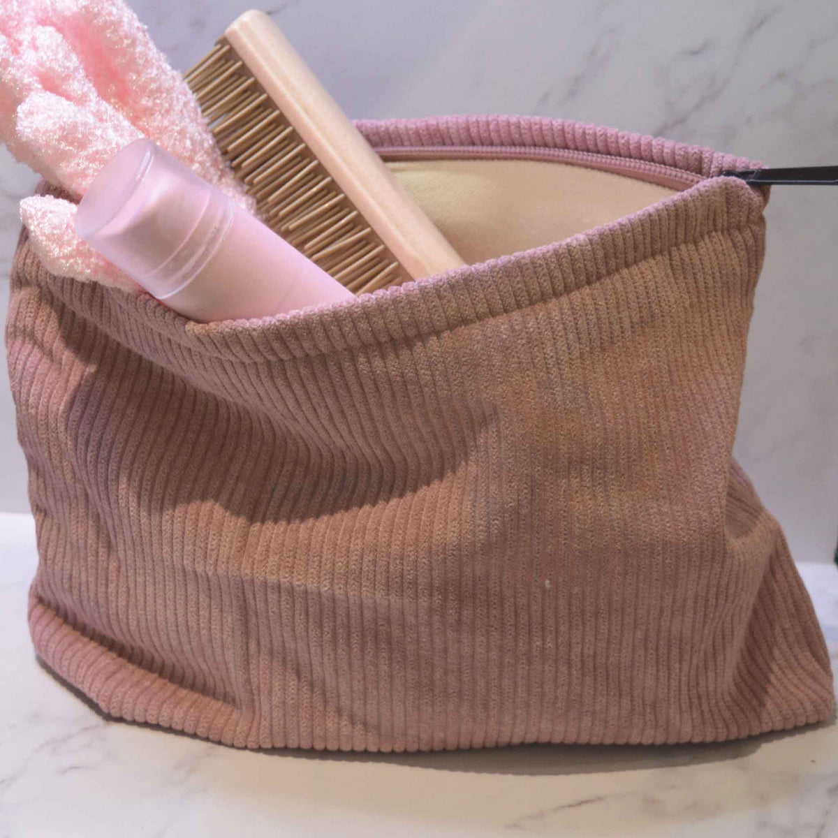 Pink corduroy bag with brush and gloves showing from open top on a white background