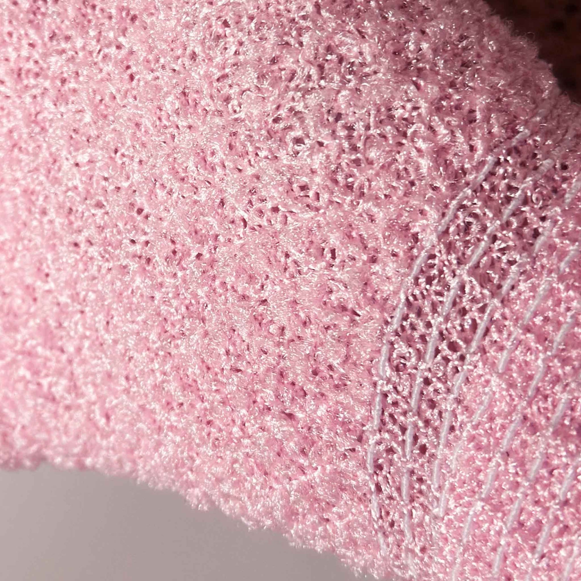 A pair of baby blue exfoliating gloves, with a pair of baby pink exfoliating gloves on a white textured background