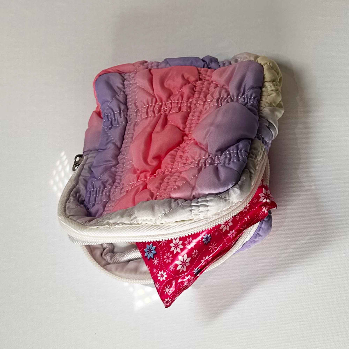 A small pink and Purple square bag open on its side showing a floral plastic bag at the opening on a white background
