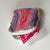 A small pink and Purple square bag open on its side showing a floral plastic bag at the opening on a white background