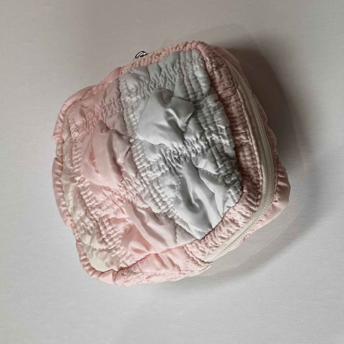 A small pale pink and blue square bag zipped close on its side on a white background