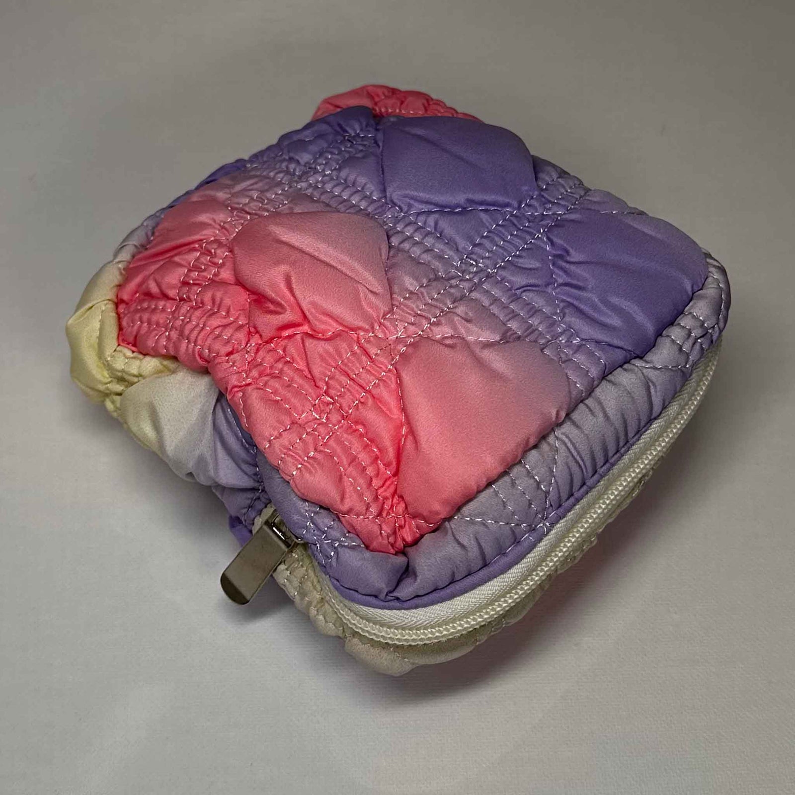 A square bag coloured with a mix of pink and purple, zipped shut on a white background