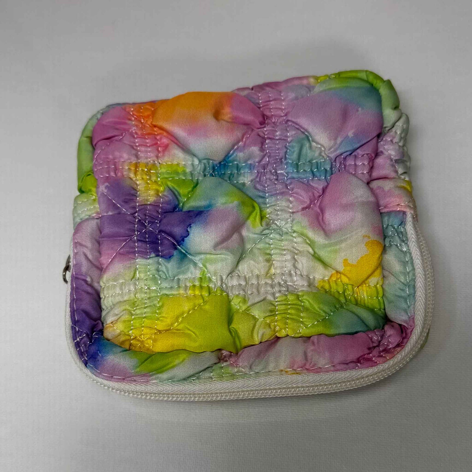 A square bag coloured with a mix of water colours, zipped shut on a white background