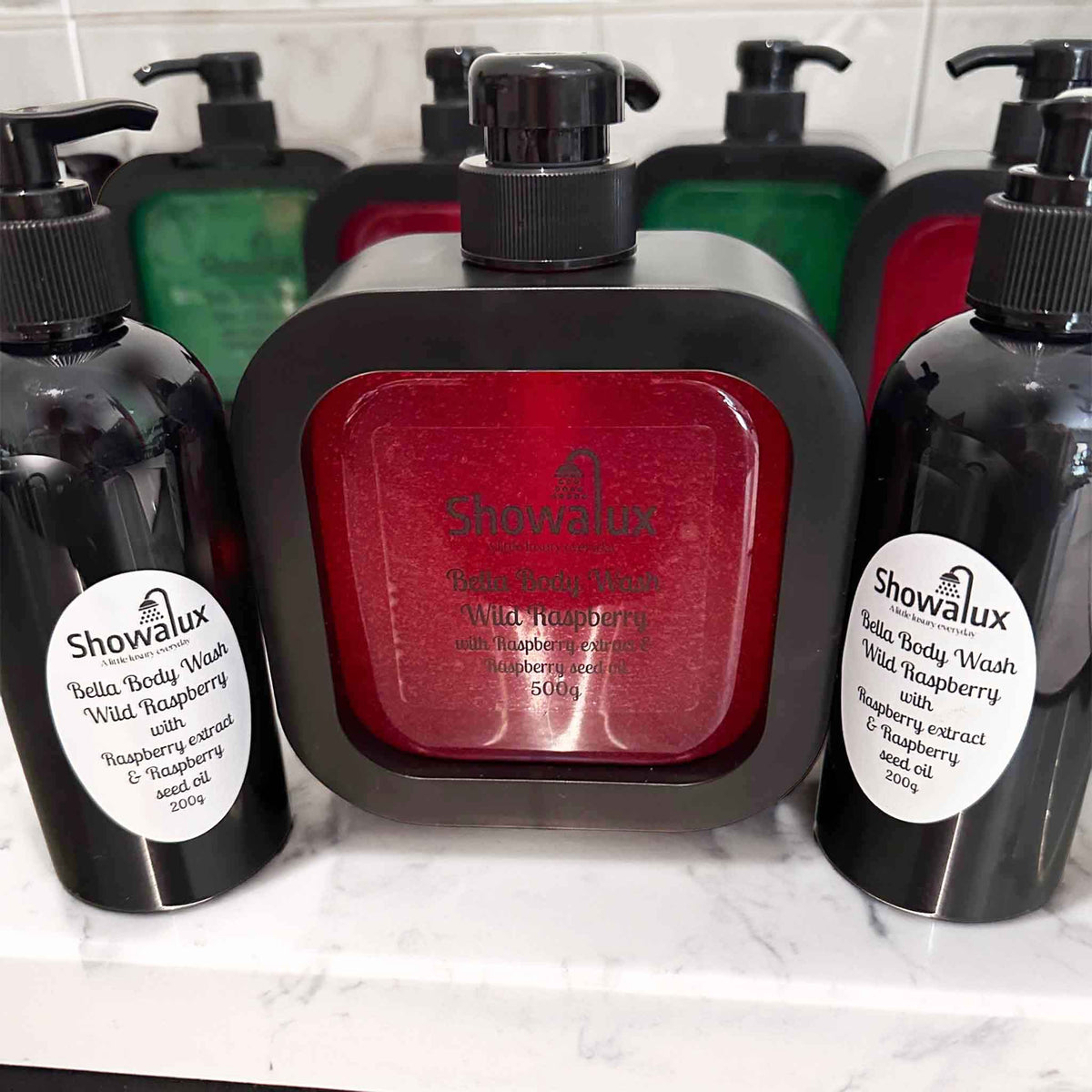 Showalux Bella Body Wash bottles with red label and black pump on a white marble surface.