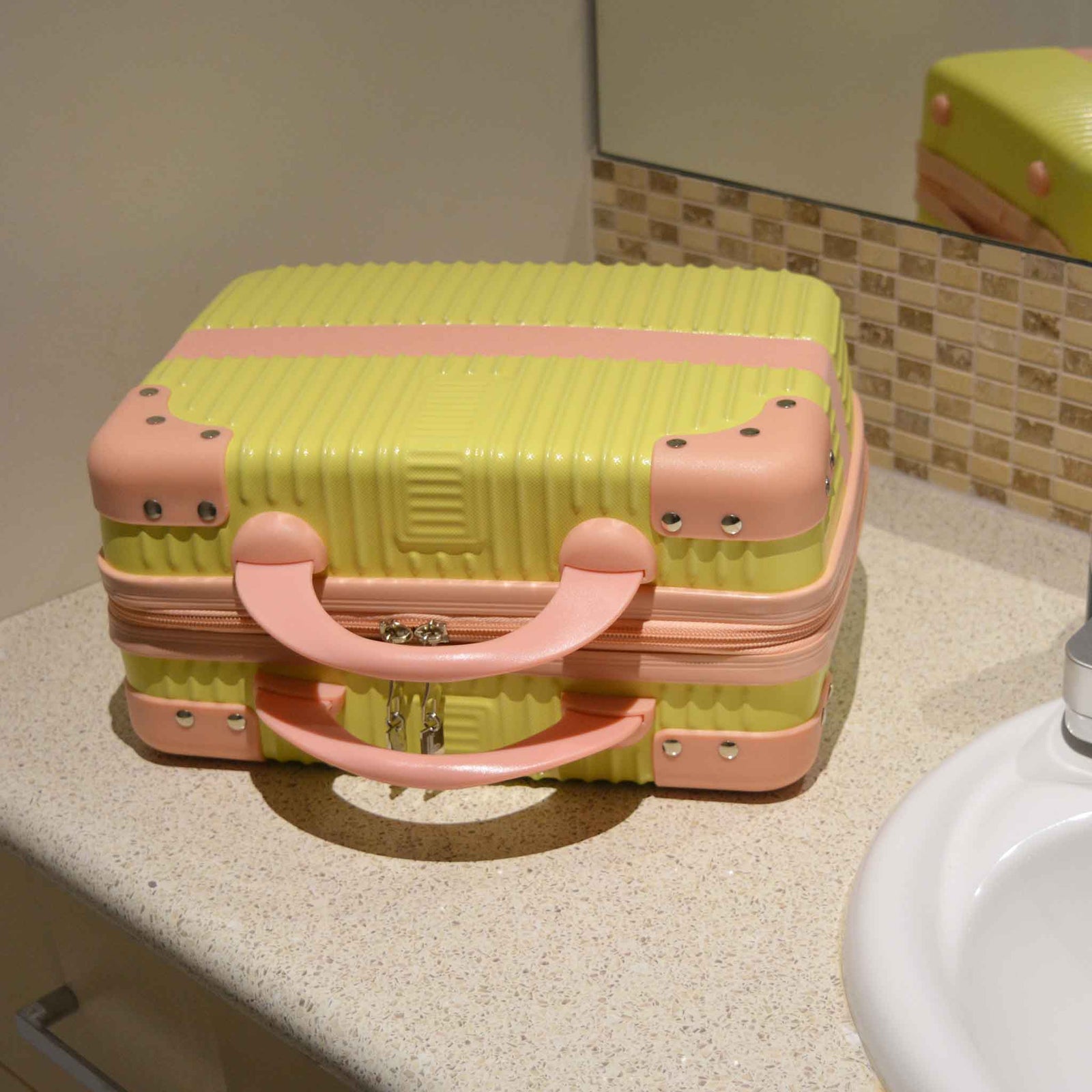 Suitcase Style Toiletry Bag closed and laying on its side on a bathroom bench. Cream case with pink corners, handles and strap