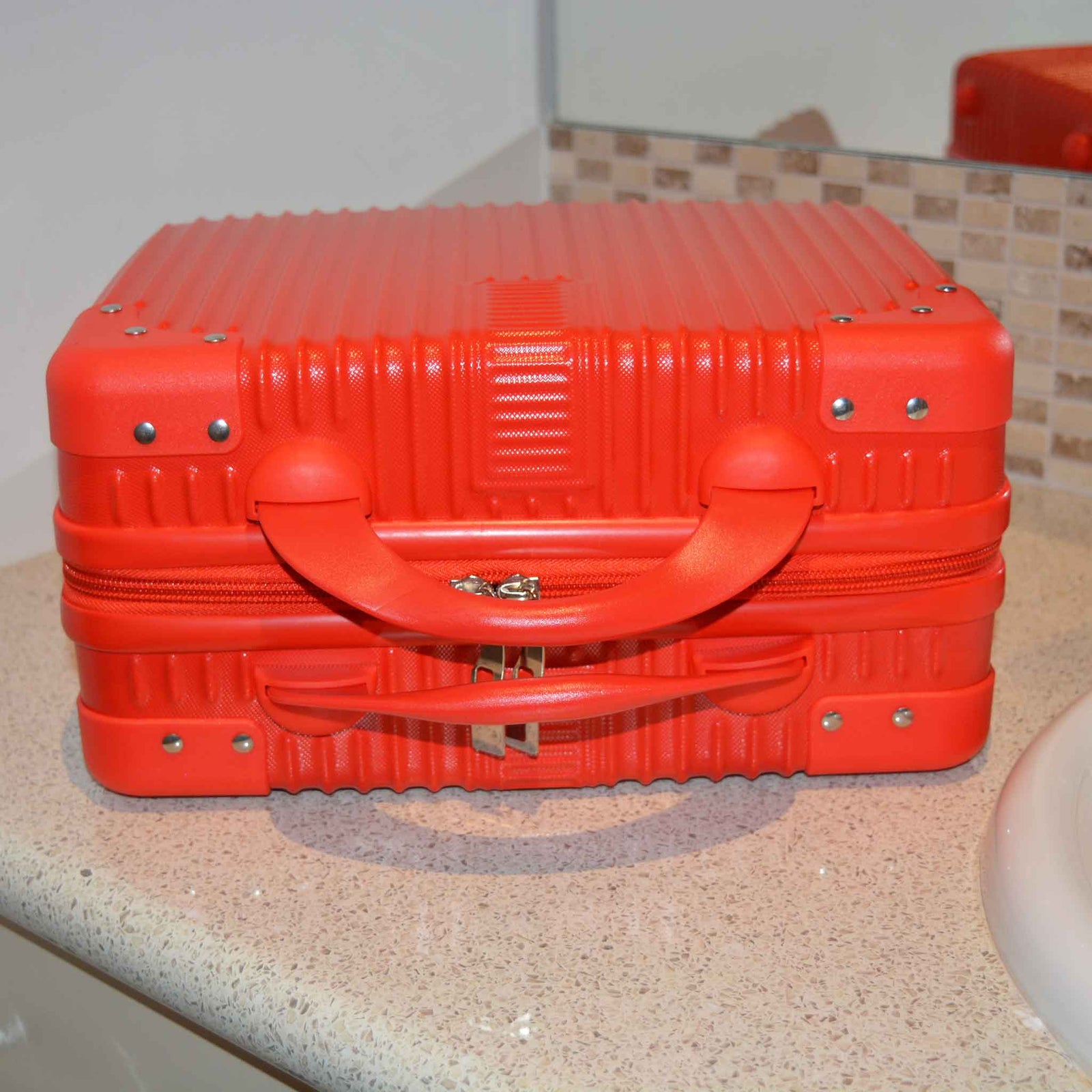 Suitcase Style Toiletry Bag closed and laying on its side on a bathroom bench in RED