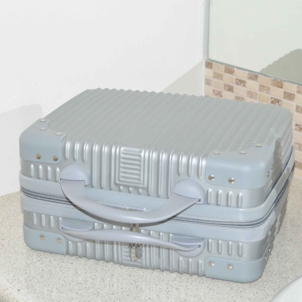 Suitcase Style Toiletry Bag closed and laying on its side on a bathroom bench in Silver