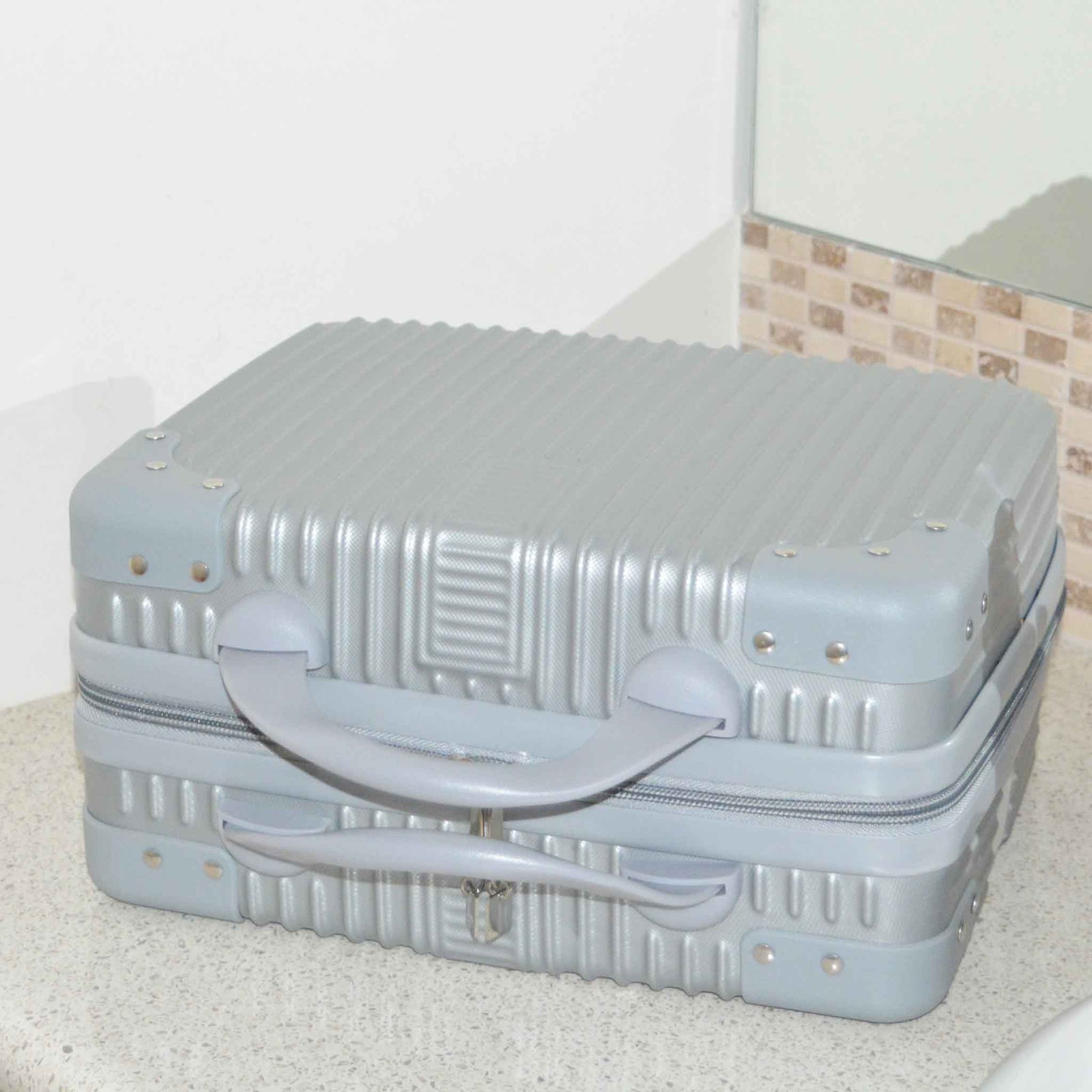 Suitcase Style Toiletry Bag closed and laying on its side on a bathroom bench in Silver