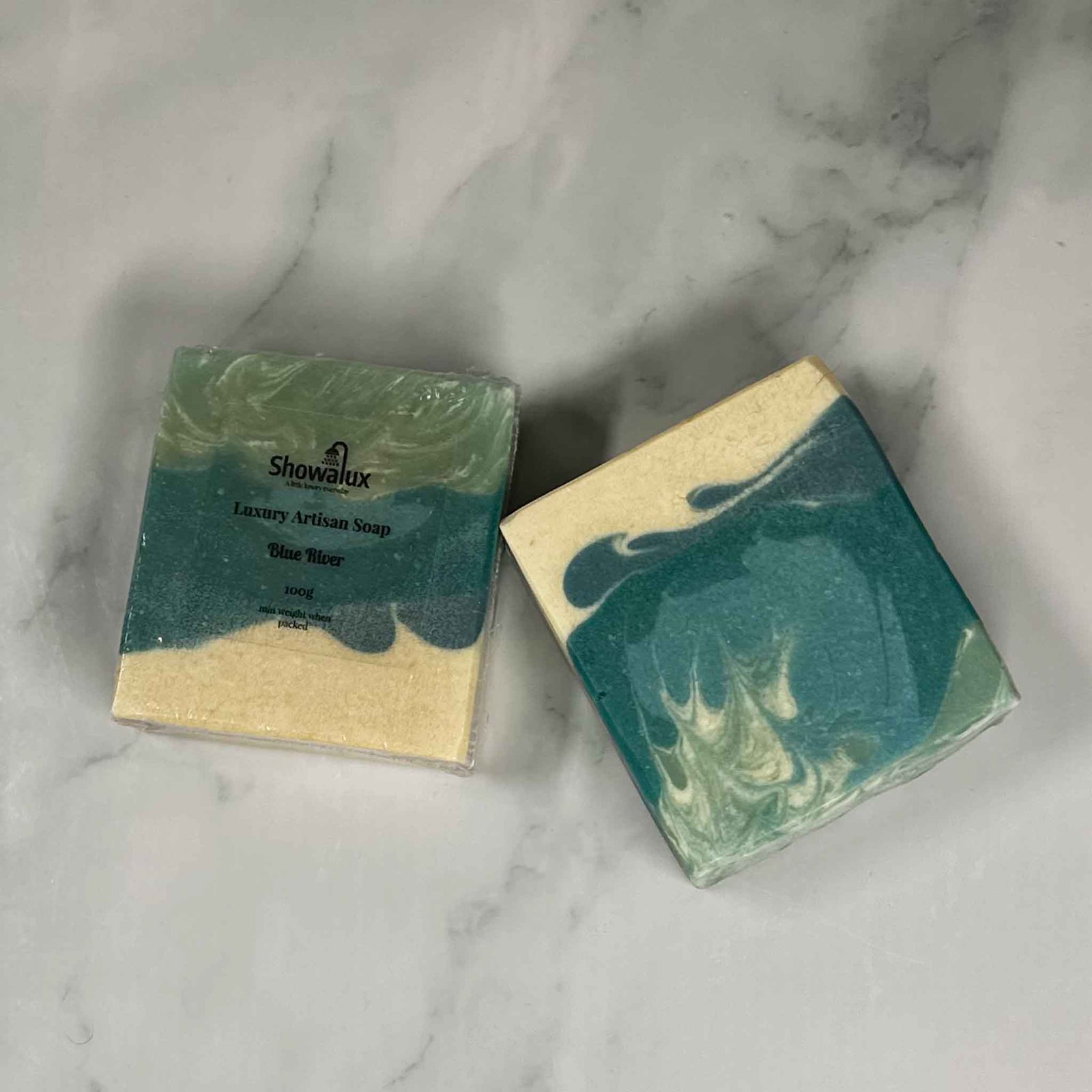 2 soap bars coloured blue, green and cream, one with a label,  on a marble background
