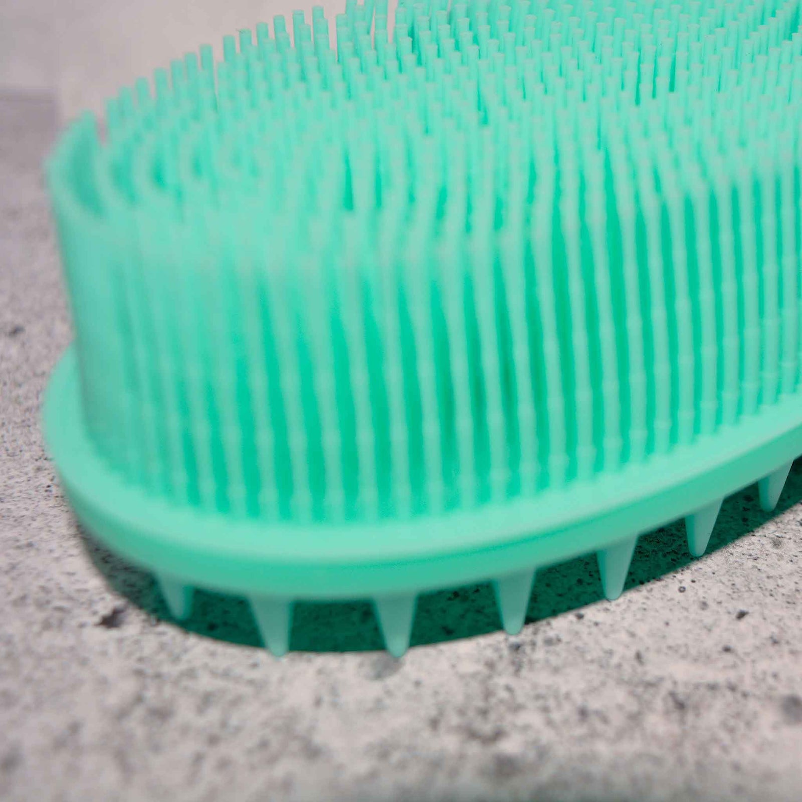 Close up of Mint green soft silicone scrub brush with very soft fine bristles on one side, and short firm nubs on the other side