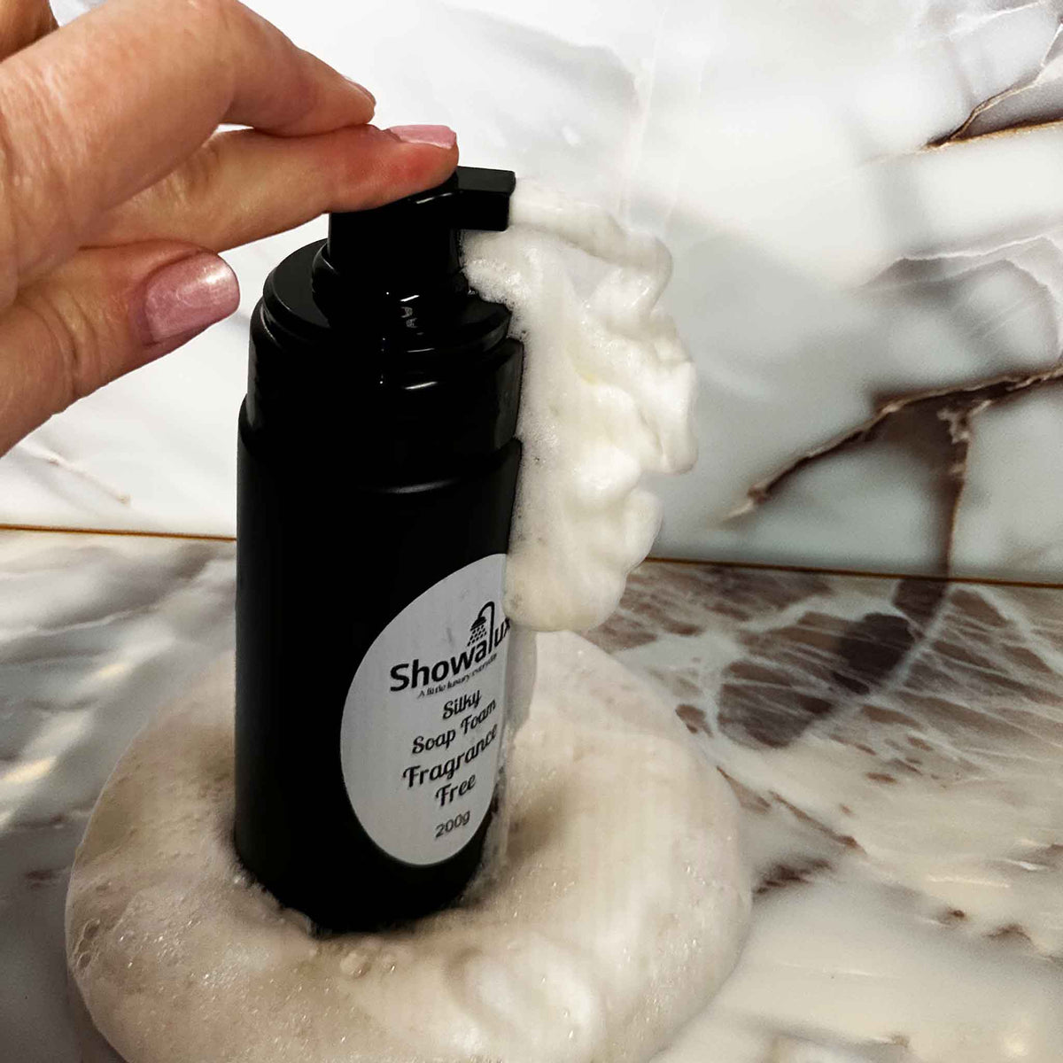 Black bottle of Showalux liquid soap with a hand applying soap on a marble surface