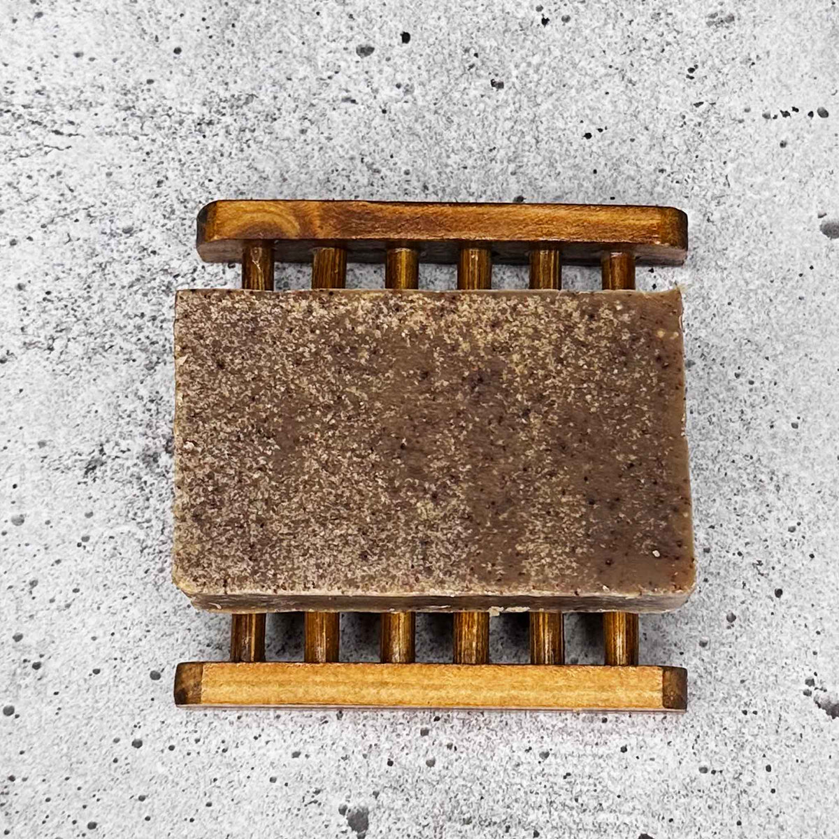 Bar of soap on a wooden soap dish against a concrete background